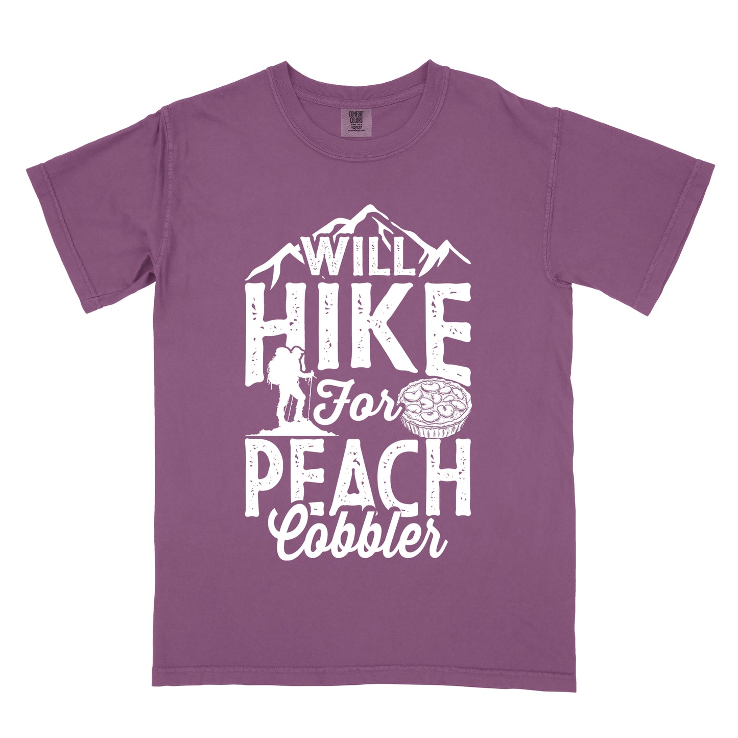 Berry (Dark Violet) t-shirt with white text reading "WILL HIKE FOR PEACH COBBLER". "WILL HIKE" appears in large distressed letters at the top with mountain silhouettes, "For" in white script across the middle, and "PEACH COBBLER" in large distressed letters at the bottom. The design includes a small hiker figure with backpack on the left and an illustration of a peach cobbler pie. The design humorously connects hiking activity with dessert motivation.