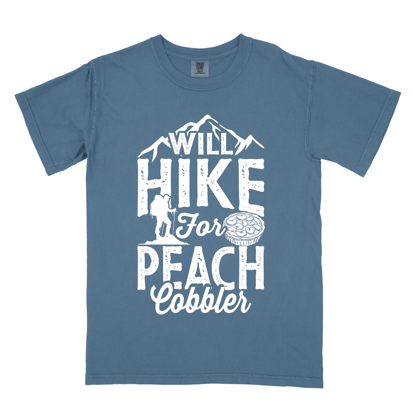 Blue Jean (Denim Blue) t-shirt with white text reading "WILL HIKE FOR PEACH COBBLER". "WILL HIKE" appears in large distressed letters at the top with mountain silhouettes, "For" in white script across the middle, and "PEACH COBBLER" in large distressed letters at the bottom. The design includes a small hiker figure with backpack on the left and an illustration of a peach cobbler pie. The design humorously connects hiking activity with dessert motivation.