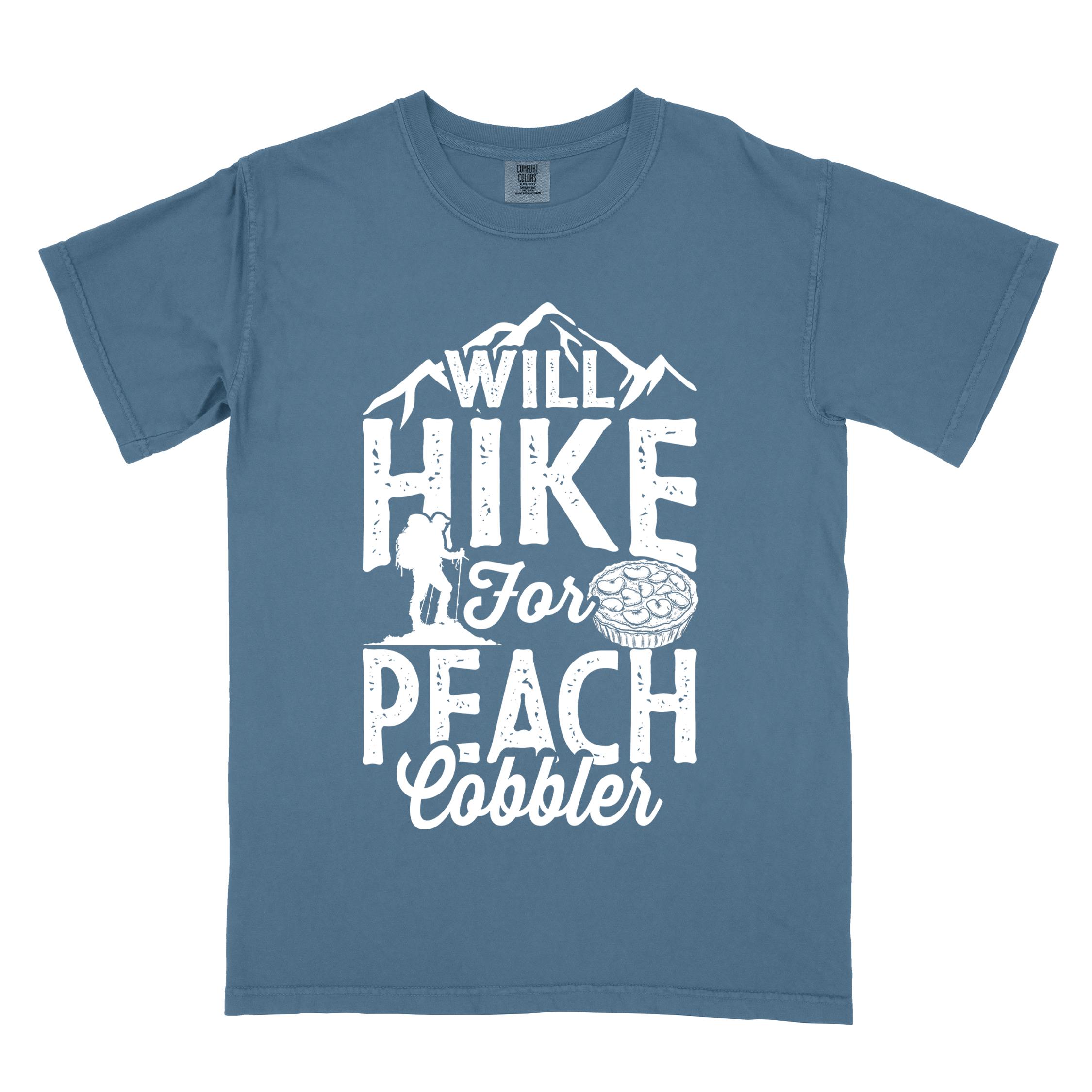 Blue jean "Will hike for peach cobbler" colored vintage tee with bold typography, mountain, birds, illustrated peach cobbler, and backpacker looking for sweet treats.