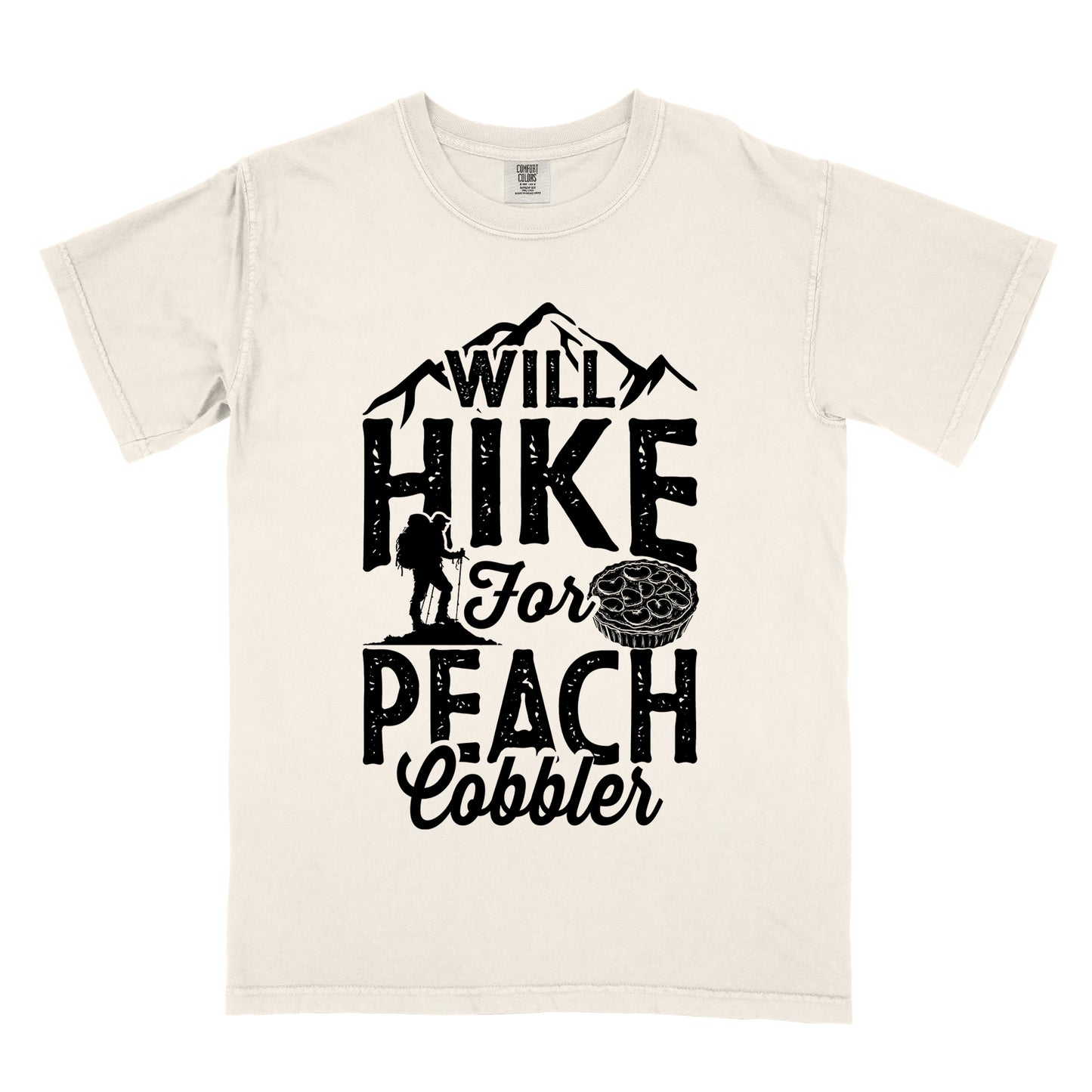 Ivory (Cream White) t-shirt with black text reading "WILL HIKE FOR PEACH COBBLER". "WILL HIKE" appears in large distressed letters at the top with mountain silhouettes, "For" in black script across the middle, and "PEACH COBBLER" in large distressed letters at the bottom. The design includes a small hiker figure with backpack on the left and an illustration of a peach cobbler pie. The design humorously connects hiking activity with dessert motivation.