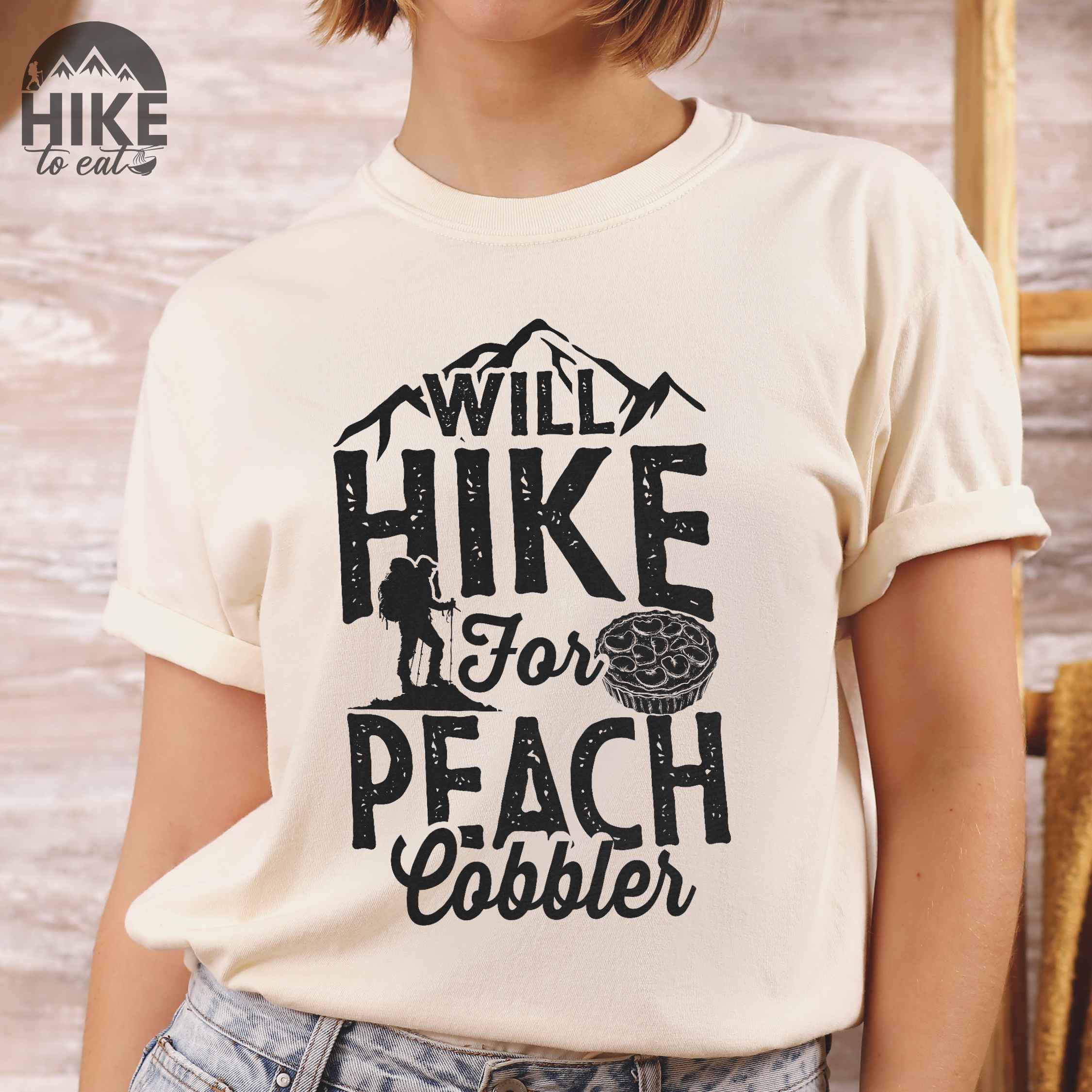 Ivory "Will hike for peach cobbler" colored vintage tee with bold typography, mountain, birds, illustrated peach cobbler, and backpacker looking for sweet treats.