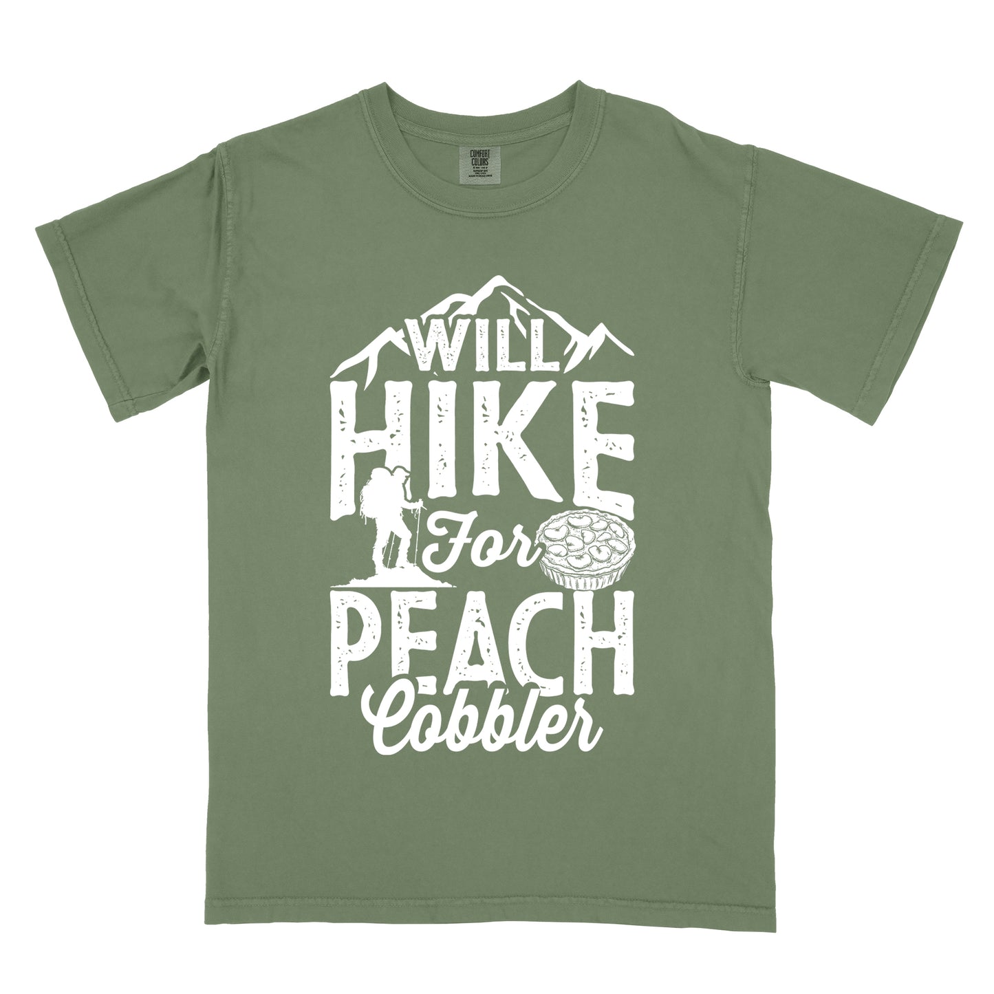 Moss (Dark Green) t-shirt with white text reading "WILL HIKE FOR PEACH COBBLER". "WILL HIKE" appears in large distressed letters at the top with mountain silhouettes, "For" in white script across the middle, and "PEACH COBBLER" in large distressed letters at the bottom. The design includes a small hiker figure with backpack on the left and an illustration of a peach cobbler pie. The design humorously connects hiking activity with dessert motivation.