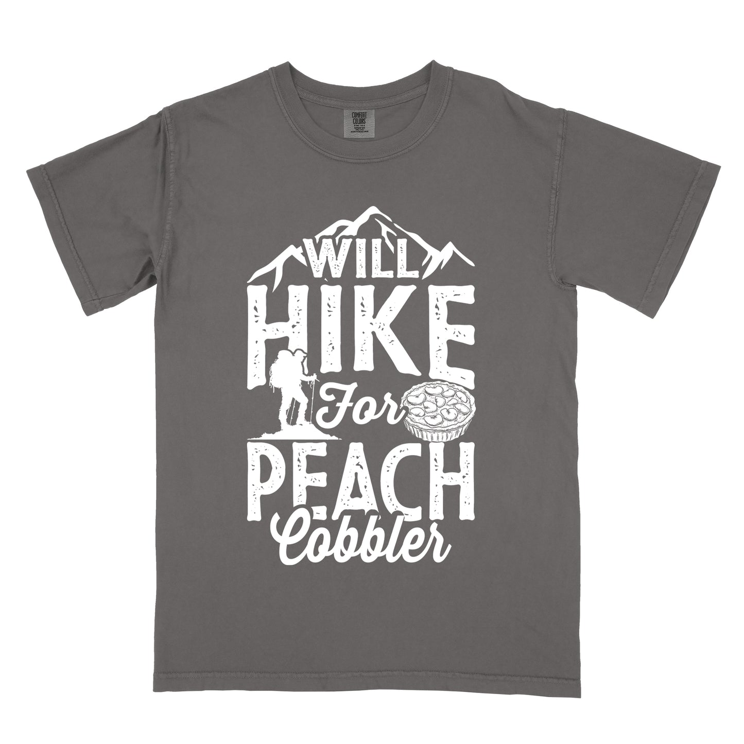 Pepper (Dark Gray) t-shirt with white text reading "WILL HIKE FOR PEACH COBBLER". "WILL HIKE" appears in large distressed letters at the top with mountain silhouettes, "For" in white script across the middle, and "PEACH COBBLER" in large distressed letters at the bottom. The design includes a small hiker figure with backpack on the left and an illustration of a peach cobbler pie. The design humorously connects hiking activity with dessert motivation.
