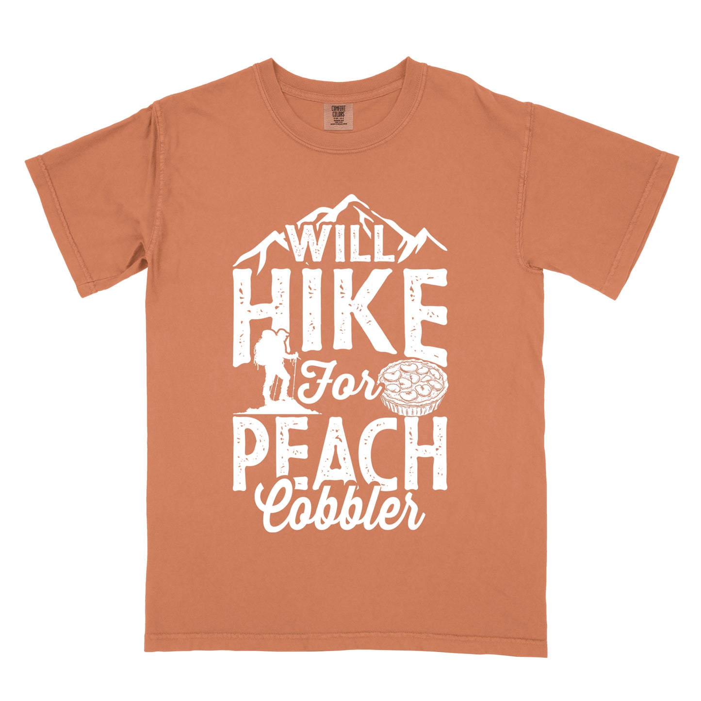 Yam (Brown) t-shirt with white text reading "WILL HIKE FOR PEACH COBBLER". "WILL HIKE" appears in large distressed letters at the top with mountain silhouettes, "For" in white script across the middle, and "PEACH COBBLER" in large distressed letters at the bottom. The design includes a small hiker figure with backpack on the left and an illustration of a peach cobbler pie. The design humorously connects hiking activity with dessert motivation.