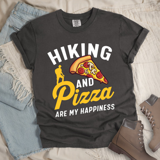 Pepper (Dark Gray) t-shirt with white and yellow text reading "HIKING AND Pizza ARE MY HAPPINESS". "HIKING" appears in white at the top, "AND" in white in the middle, "Pizza" in yellow script, and "ARE MY HAPPINESS" in white at the bottom. Features a colorful pizza slice with pepperoni and mushrooms in the center-right and a yellow silhouette of a hiker on the left side above "AND Pizza ARE MY HAPPINESS". The design combines outdoor activity with food enjoyment.