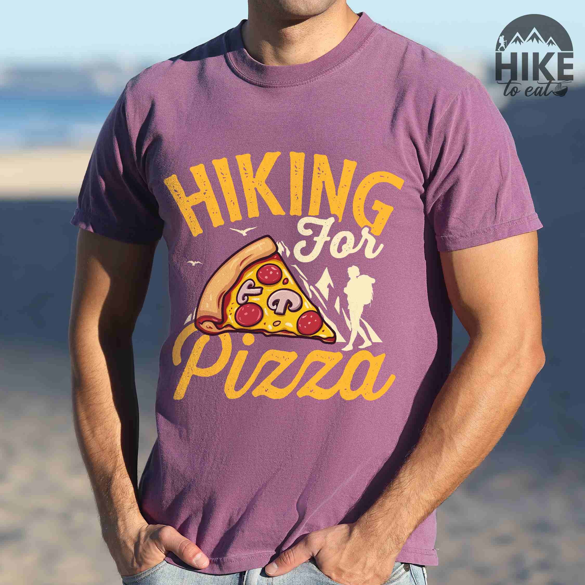 man wearing berry "Hiking for Pizza" colored vintage tee with bold typography, birds, mountains, illustrated pizza slice, and backpacker for pizza lovers.