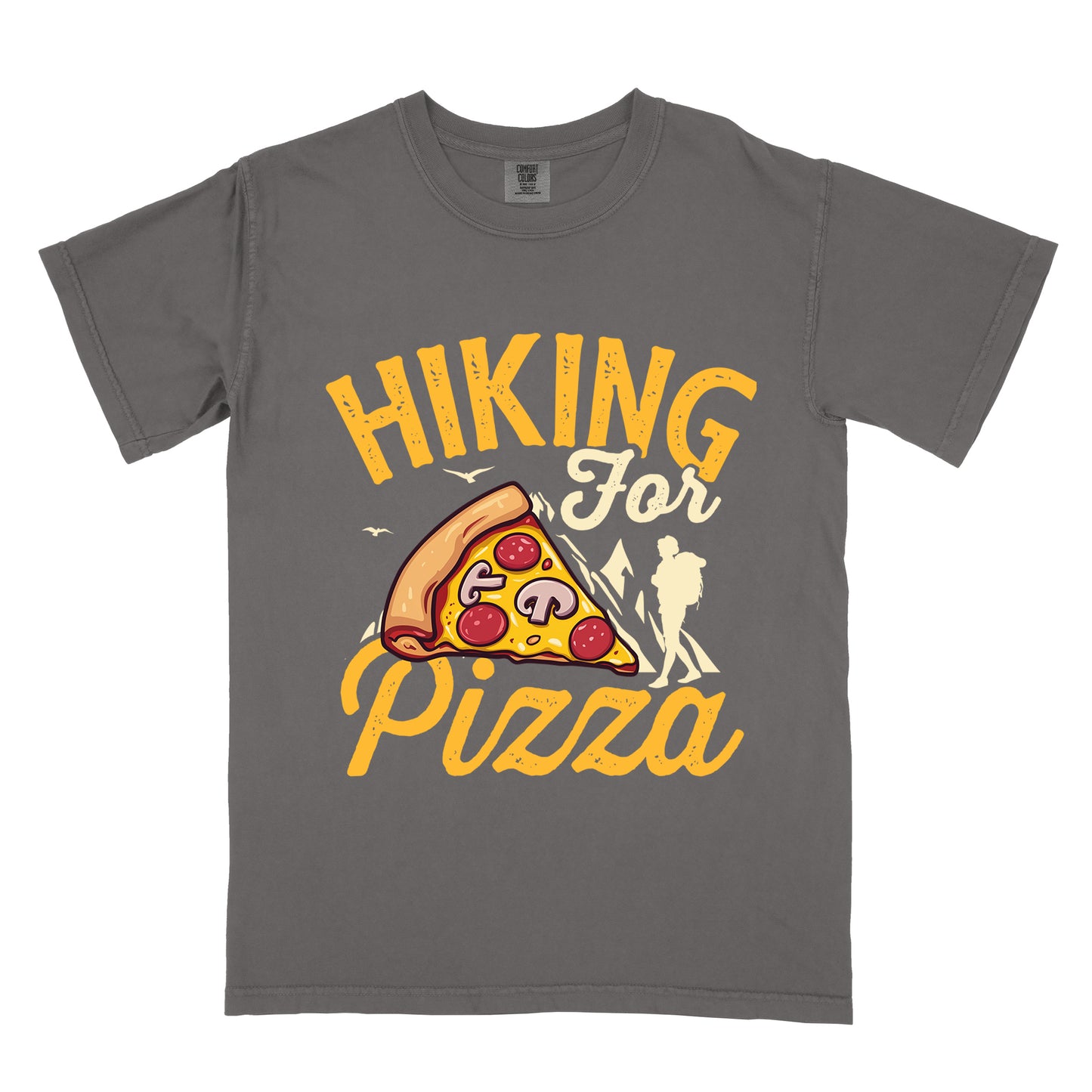 Pepper (Dark Gray) t-shirt with yellow distressed text reading "HIKING For Pizza". "HIKING" appears in large yellow letters at the top, "For" in cream script in the middle, and "Pizza" in yellow script at the bottom. Features a detailed pizza slice with pepperoni and mushrooms in the center and a cream silhouette of a hiker on the right side against mountain outlines. Small bird silhouettes appear near the mountains. The design connects hiking activity with food reward.