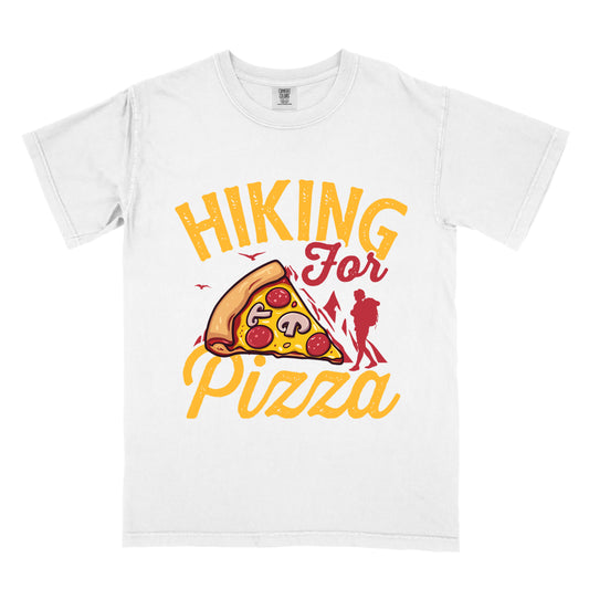 White t-shirt with yellow distressed text reading "HIKING For Pizza". "HIKING" appears in large yellow letters at the top, "For" in red script in the middle, and "Pizza" in yellow script at the bottom. Features a detailed pizza slice with pepperoni and mushrooms in the center and a red silhouette of a hiker on the right side against mountain outlines. Small bird silhouettes appear near the mountains. The design connects hiking activity with food reward.