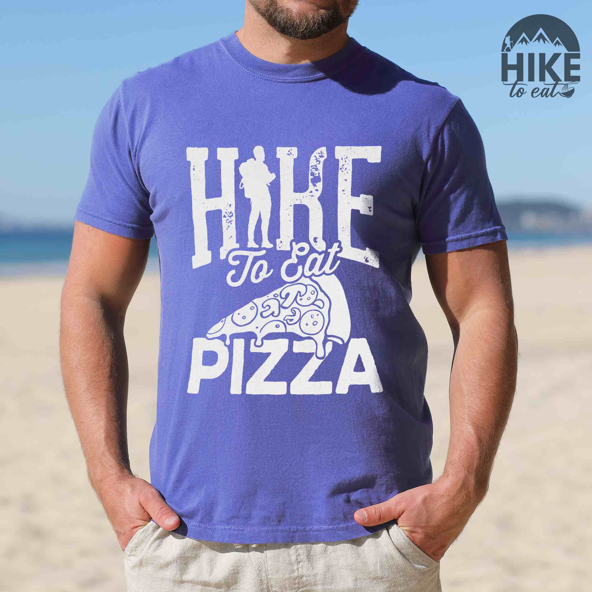 Man wearing flo blue "Hike to eat Pizza" colored vintage tee with bold typography, birds, mountains, illustrated pizza slice, and backpacker for pizza lover.