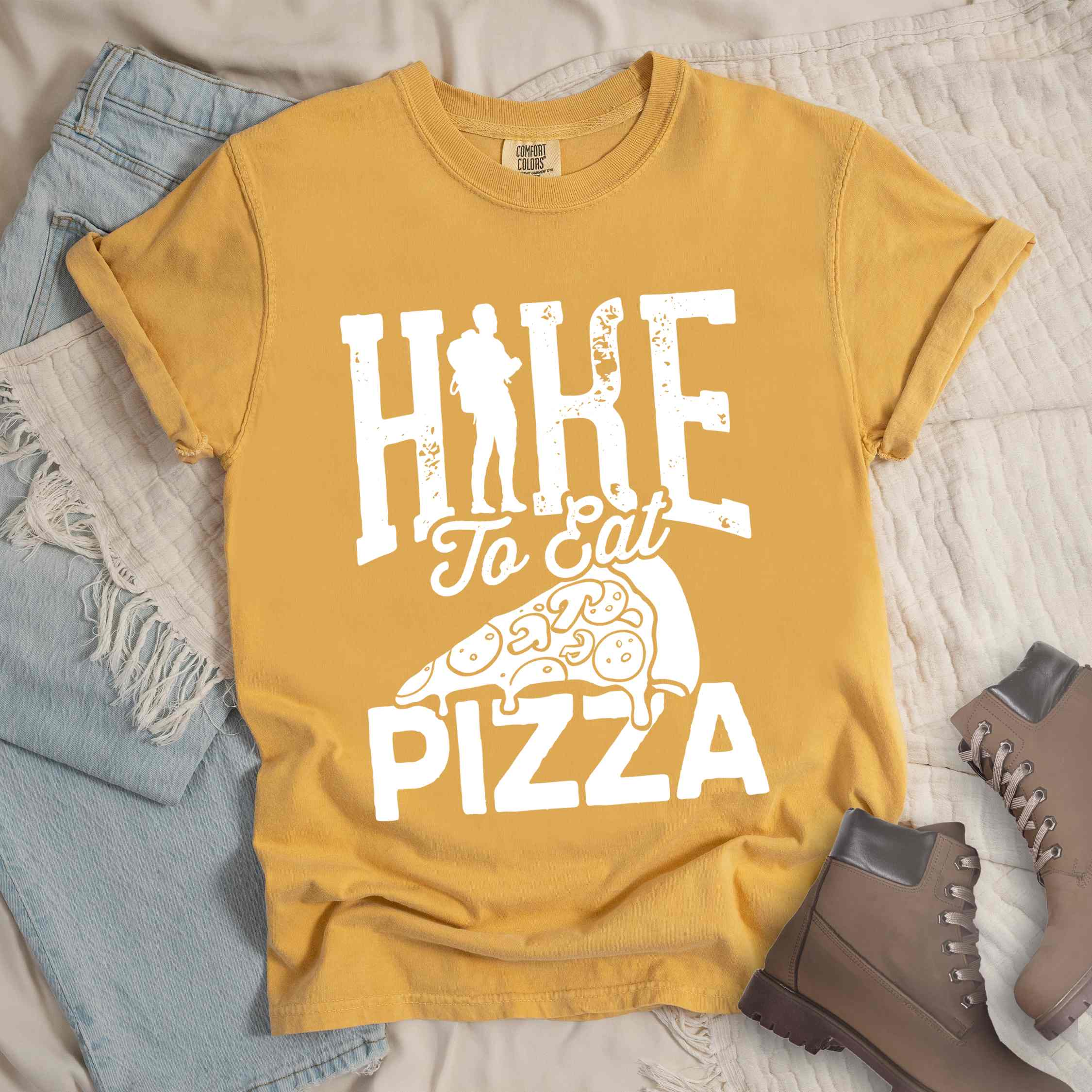 Mustard "Hike to eat Pizza" colored vintage tee with bold typography, birds, mountains, illustrated pizza slice, and backpacker for pizza lover.