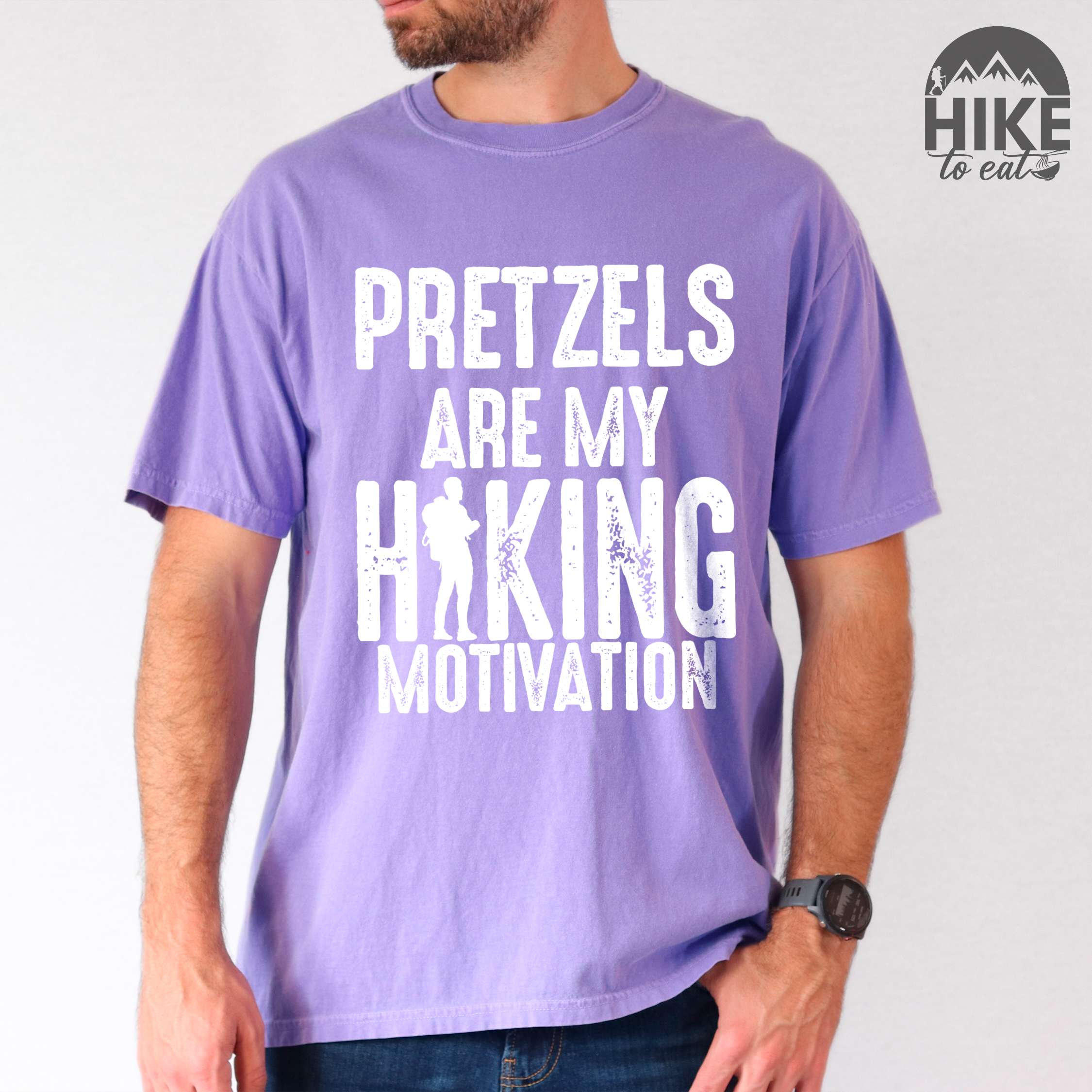 Man wearing violet "Pretzels are my hiking motivation" colored vintage tee with bold typography, and backpacker for pretzel lovers.