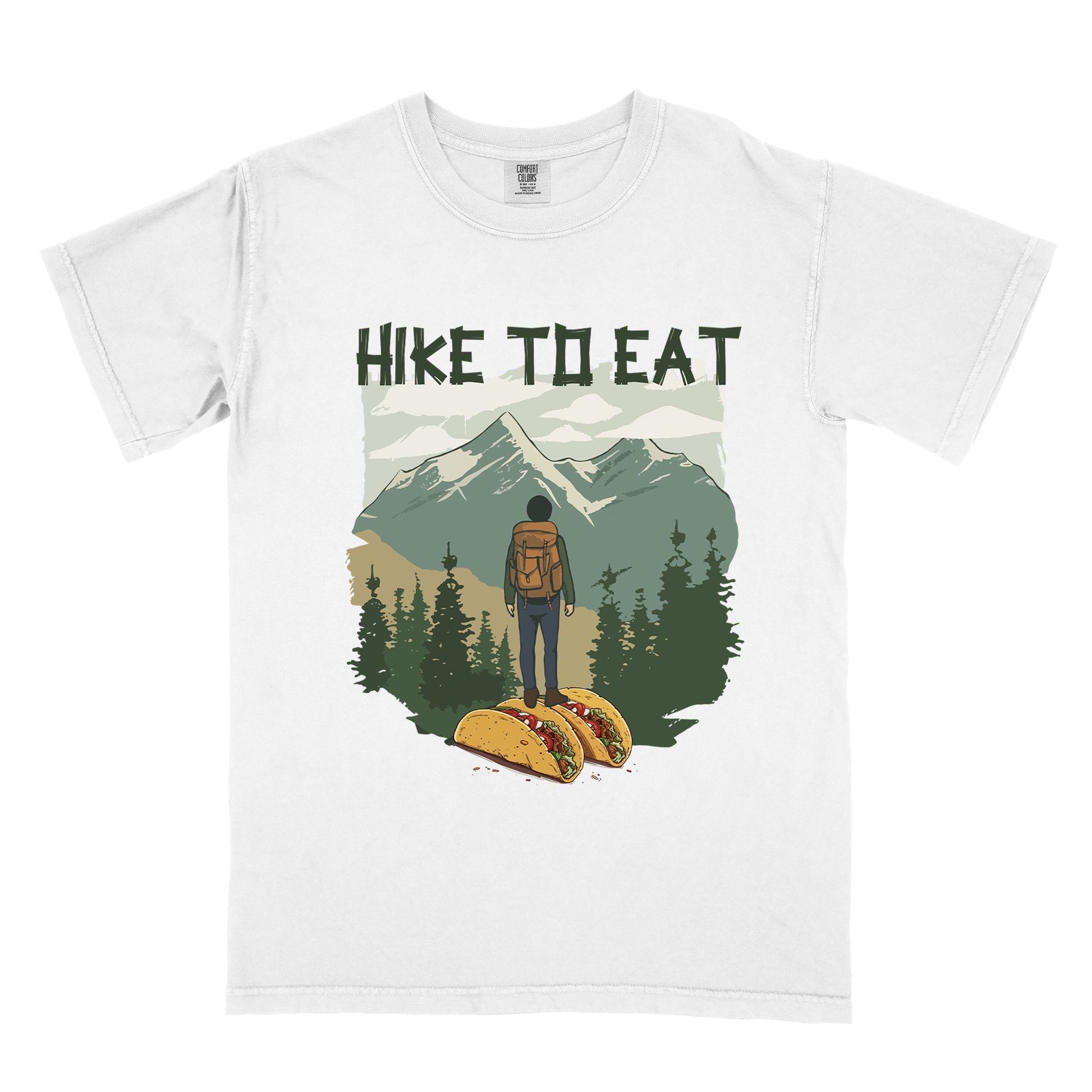 White t-shirt with "HIKE TO EAT" printed at the top in dark green text. The main graphic shows a hiker with backpack standing on two tacos, facing a scenic mountain landscape with pine trees in the foreground and snow-capped peaks in the background.