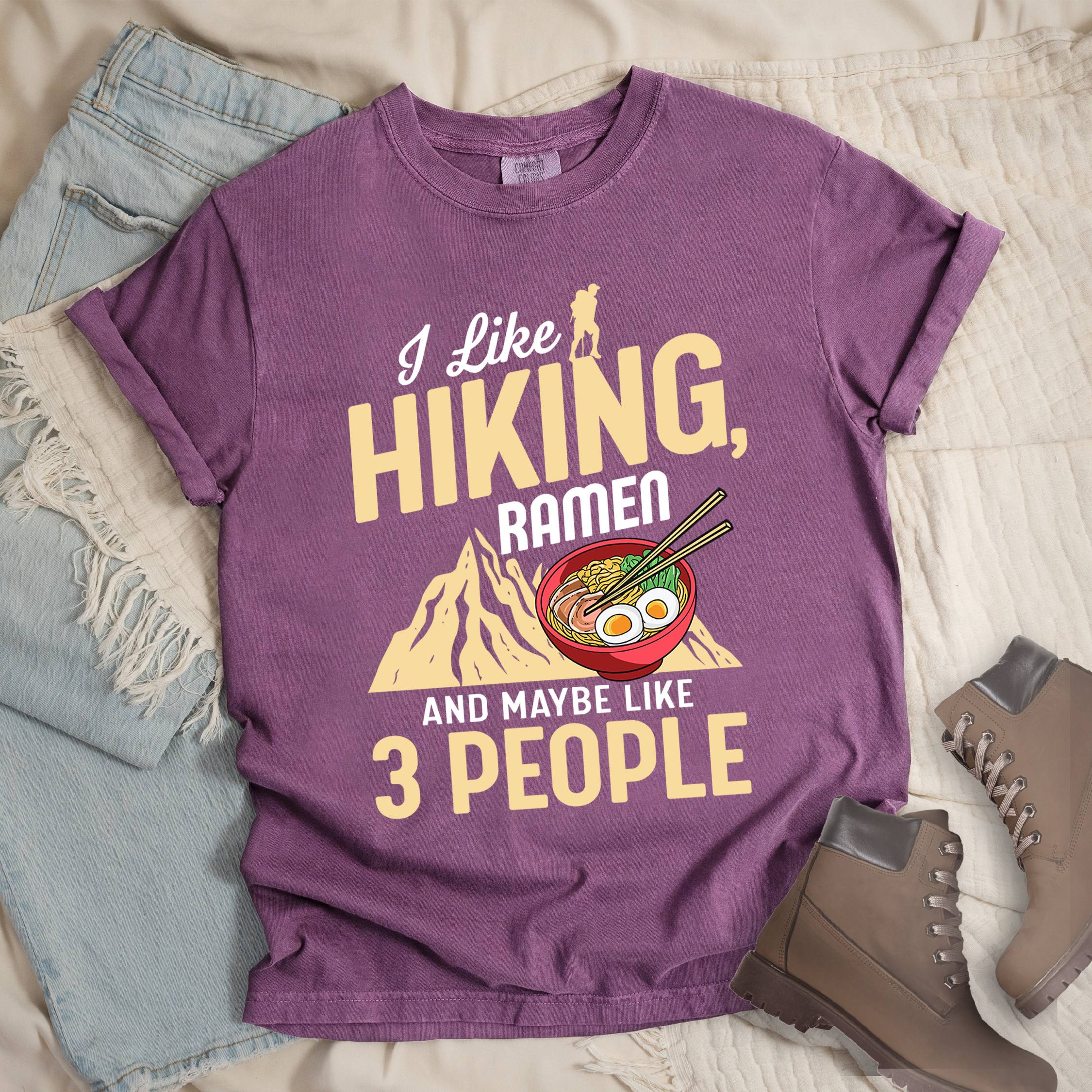 Dark pink shirt with Hiking Design featuring the phrase “I Like Hiking, Ramen, and Maybe Like 3 People” and an illustration of a steaming ramen bowl with chopsticks over a mountain outline.
