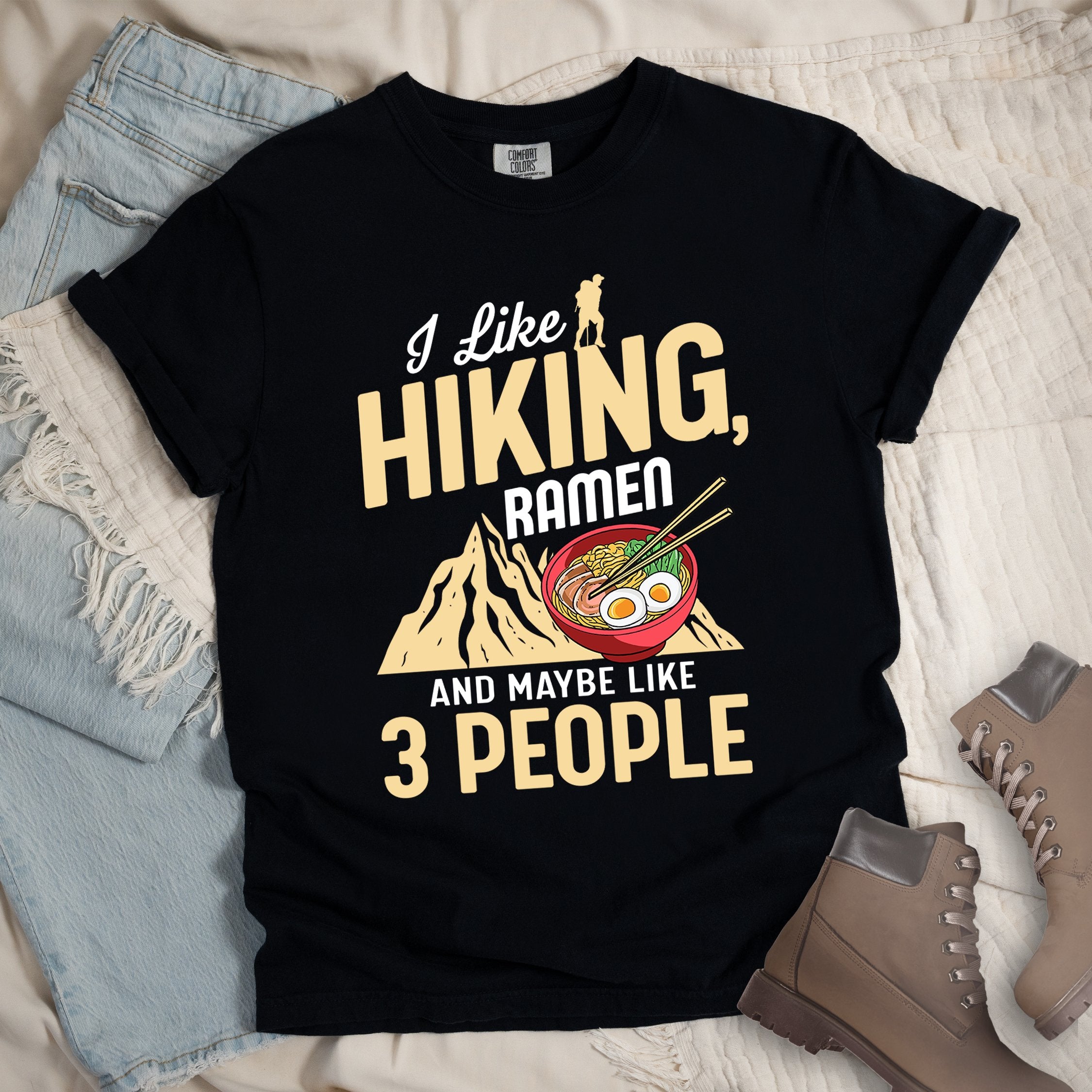 Black shirt with Hiking Design featuring the phrase “I Like Hiking, Ramen, and Maybe Like 3 People” and an illustration of a steaming ramen bowl with chopsticks over a mountain outline.