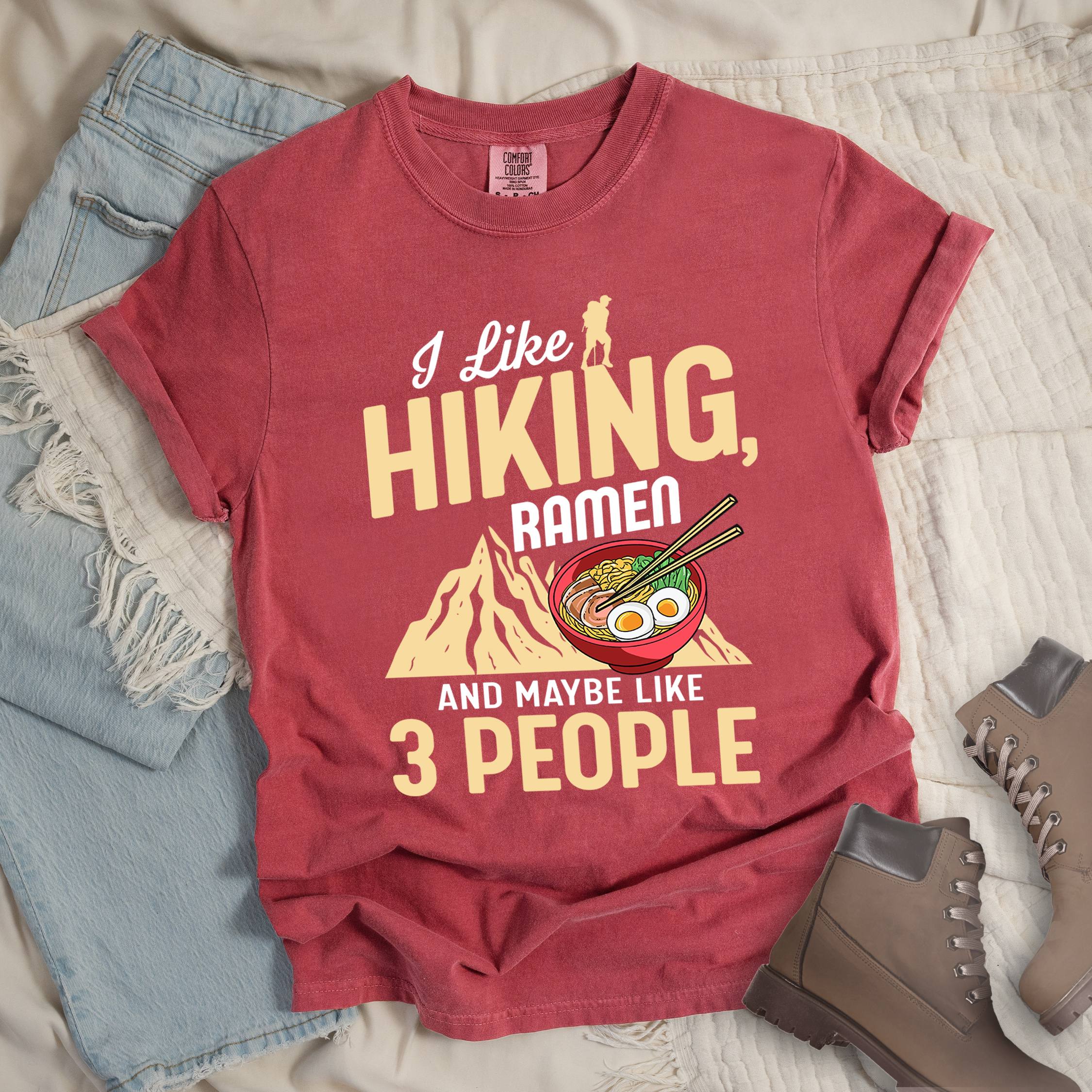 Red shirt with Hiking Design featuring the phrase “I Like Hiking, Ramen, and Maybe Like 3 People” and an illustration of a steaming ramen bowl with chopsticks over a mountain outline.