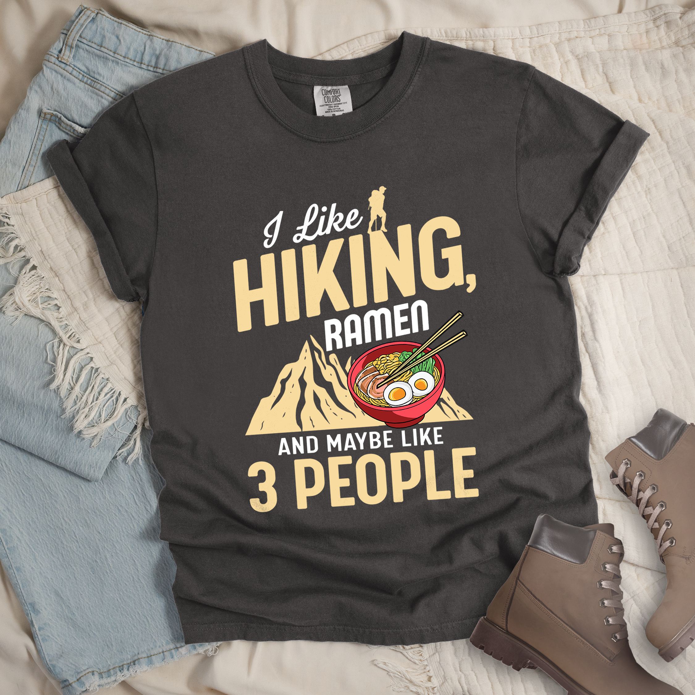 Dark grey shirt with Hiking Design featuring the phrase “I Like Hiking, Ramen, and Maybe Like 3 People” and an illustration of a steaming ramen bowl with chopsticks over a mountain outline.
