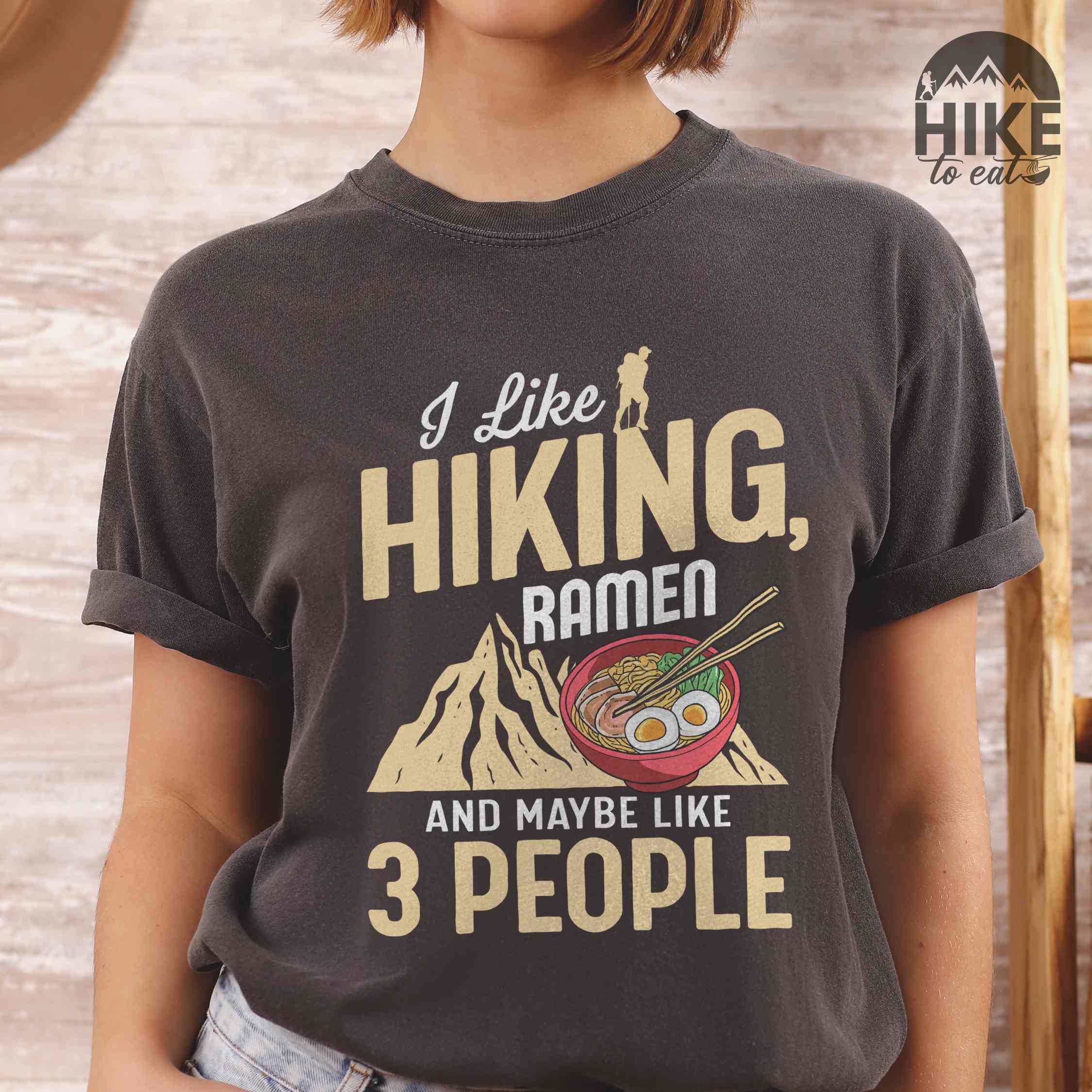 Woman wearing pepper “Ramen is my Hiking motivation” colored vintage tee with bold text, mountain, Illustration of hot ramen. Perfect tee for a foodie craving for a bowl of ramen,