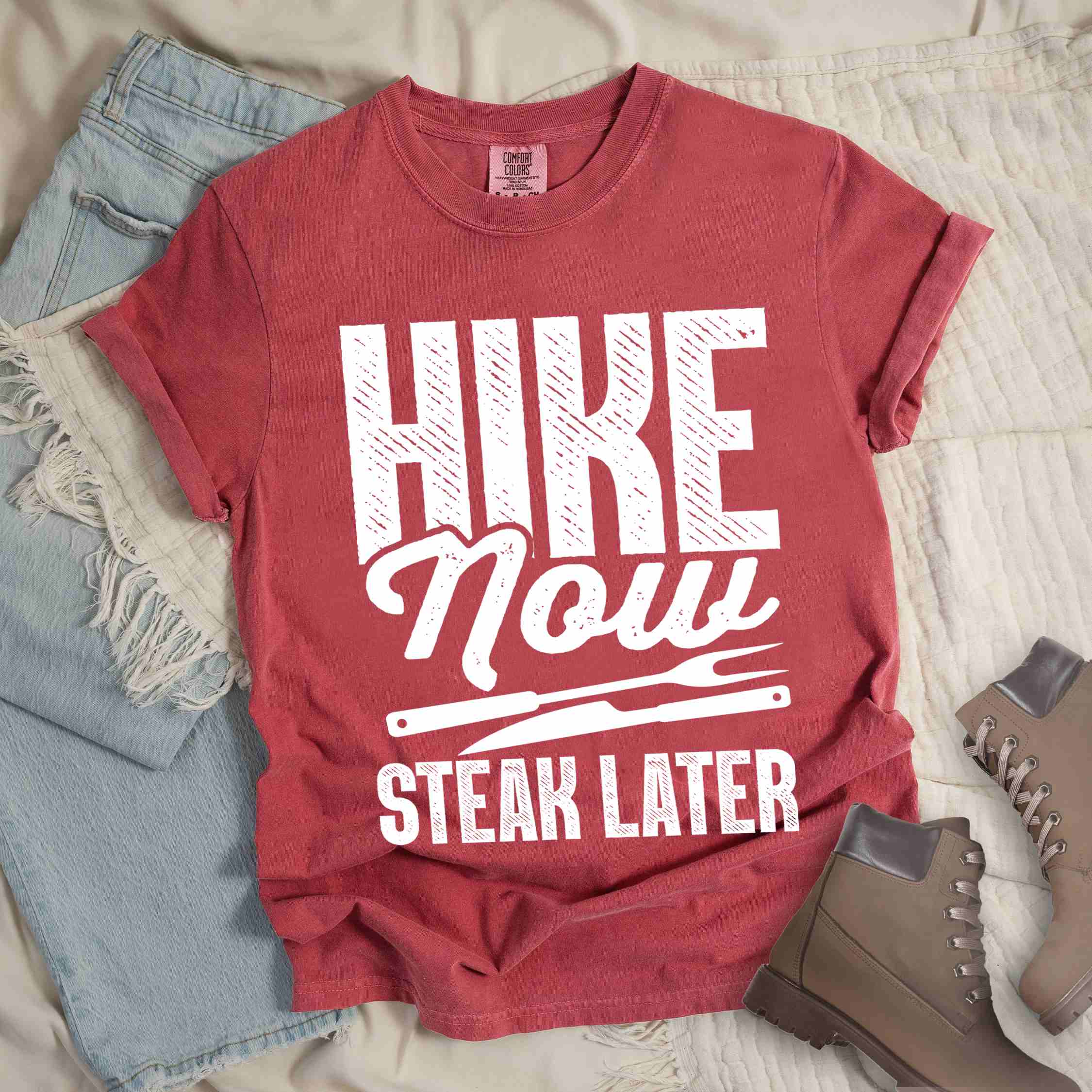 Crimson "Hike now steak later" colored vintage tee with bold typography, illustrated steak utensils, and backpacker for steak lovers.