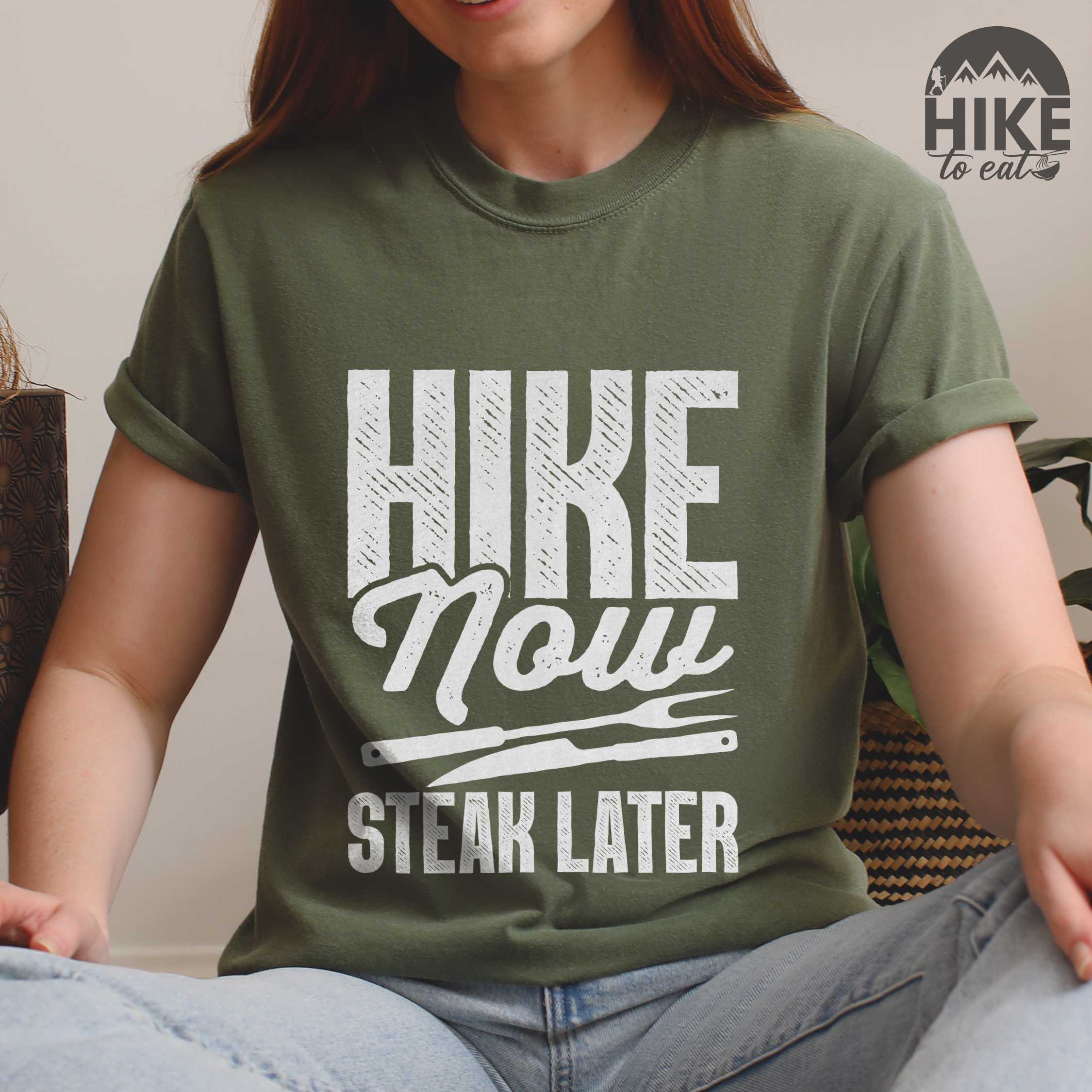 woman wearing moss "Hike now steak later" colored vintage tee with bold typography, illustrated steak utensils, and backpacker for steak lovers.