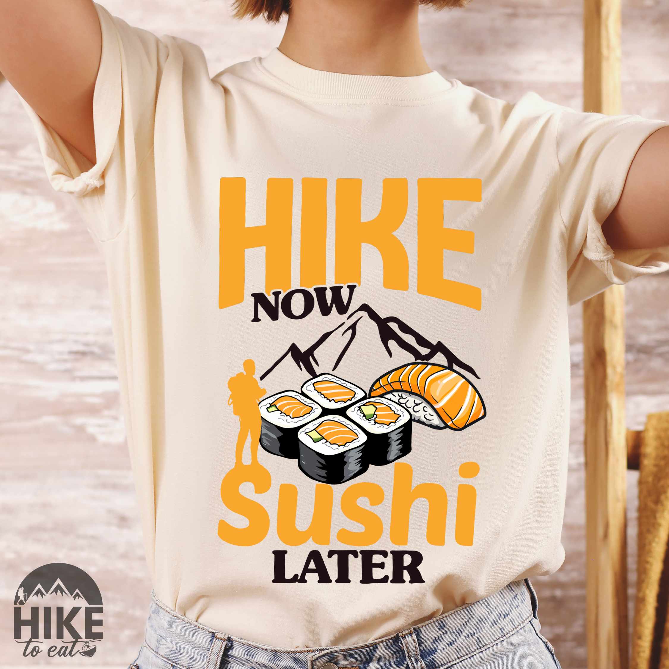 Woman wearing ivory "Hike now sushi later" colored vintage tee with bold typography, birds, mountains, illustrated sushi platter, and backpacker for sushi lovers.