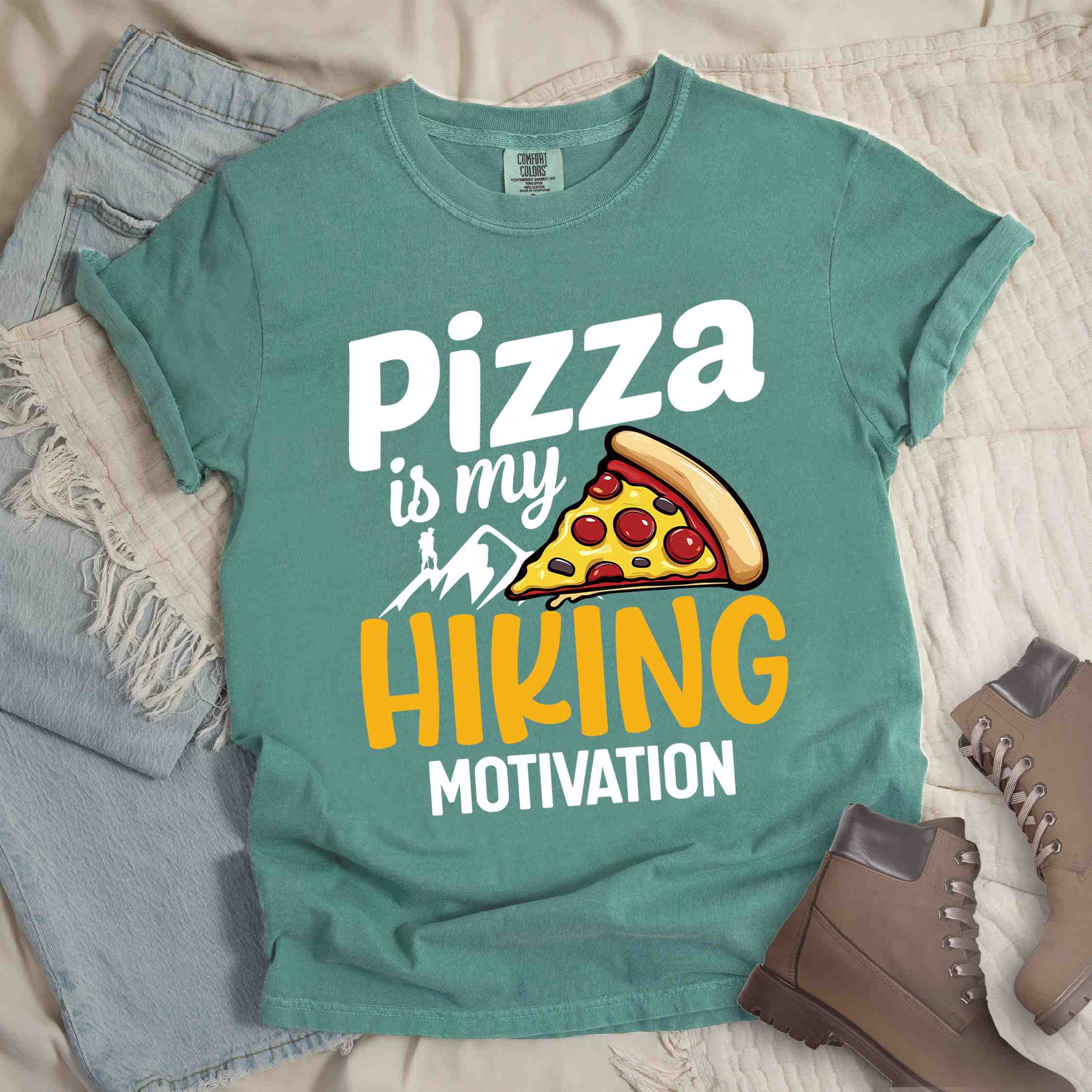 Light green "Pizza is my hiking motivation" colored vintage tee with bold typography, birds, mountains, illustrated pizza slice, and backpacker for pizza lovers.