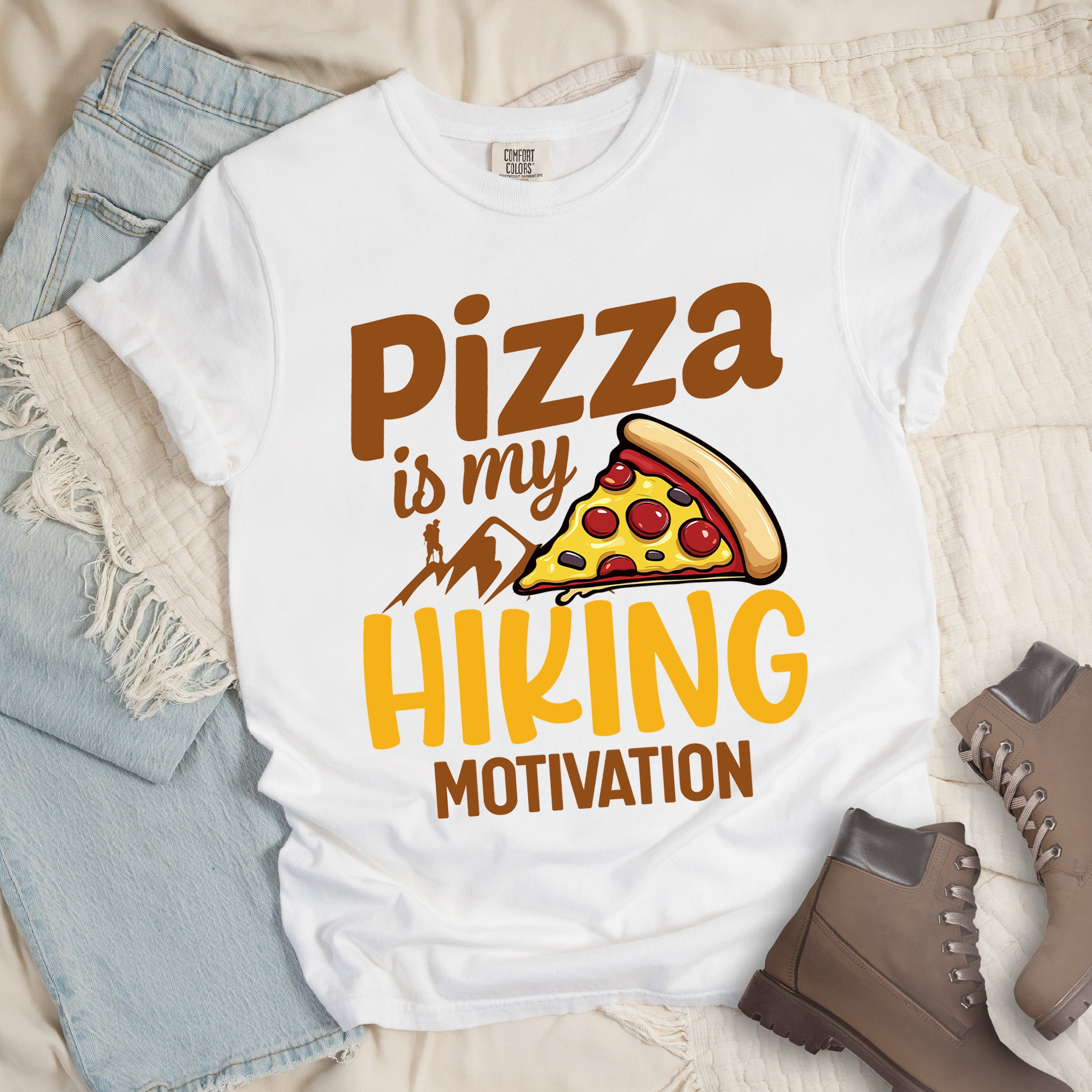 White t-shirt with brown and yellow text reading "Pizza is my HIKING MOTIVATION". "Pizza" appears in large brown letters at the top, "is my" in smaller brown script, "HIKING" in yellow at the bottom, and "MOTIVATION" in brown. Features a colorful pizza slice with pepperoni toppings, brown mountain silhouettes with a small hiker figure on a peak. The design humorously connects pizza as the incentive for hiking activities. 