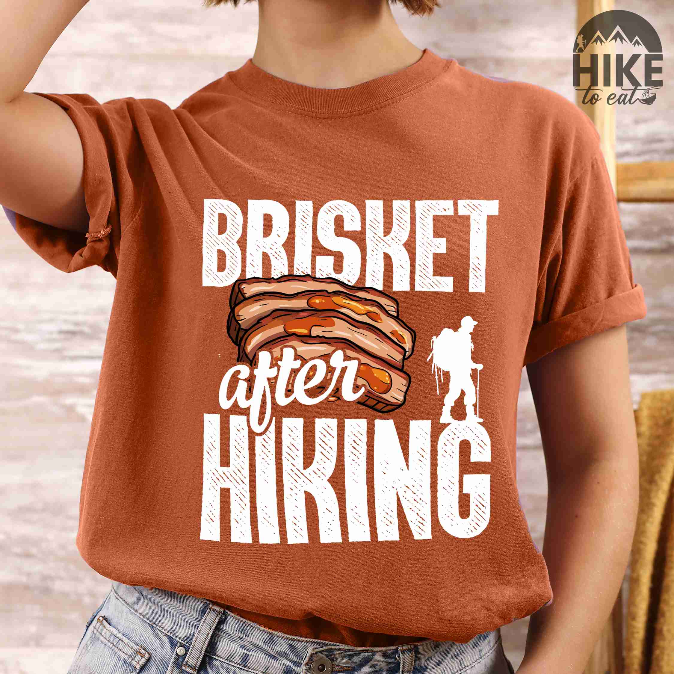 Woman wearing yam "Brisket after hiking" colored vintage tee with bold typography, birds, mountains, illustrated bbq beef brisket, and backpacker for bbq lovers.