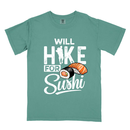 Light Green t-shirt with white distressed text reading "WILL HIKE FOR Sushi". "WILL" appears at the top, "HIKE" in large letters with a hiker silhouette integrated into the "I", "FOR" in smaller text, and "Sushi" in stylized script at the bottom. Features colorful sushi illustrations including a salmon nigiri and a maki roll. 