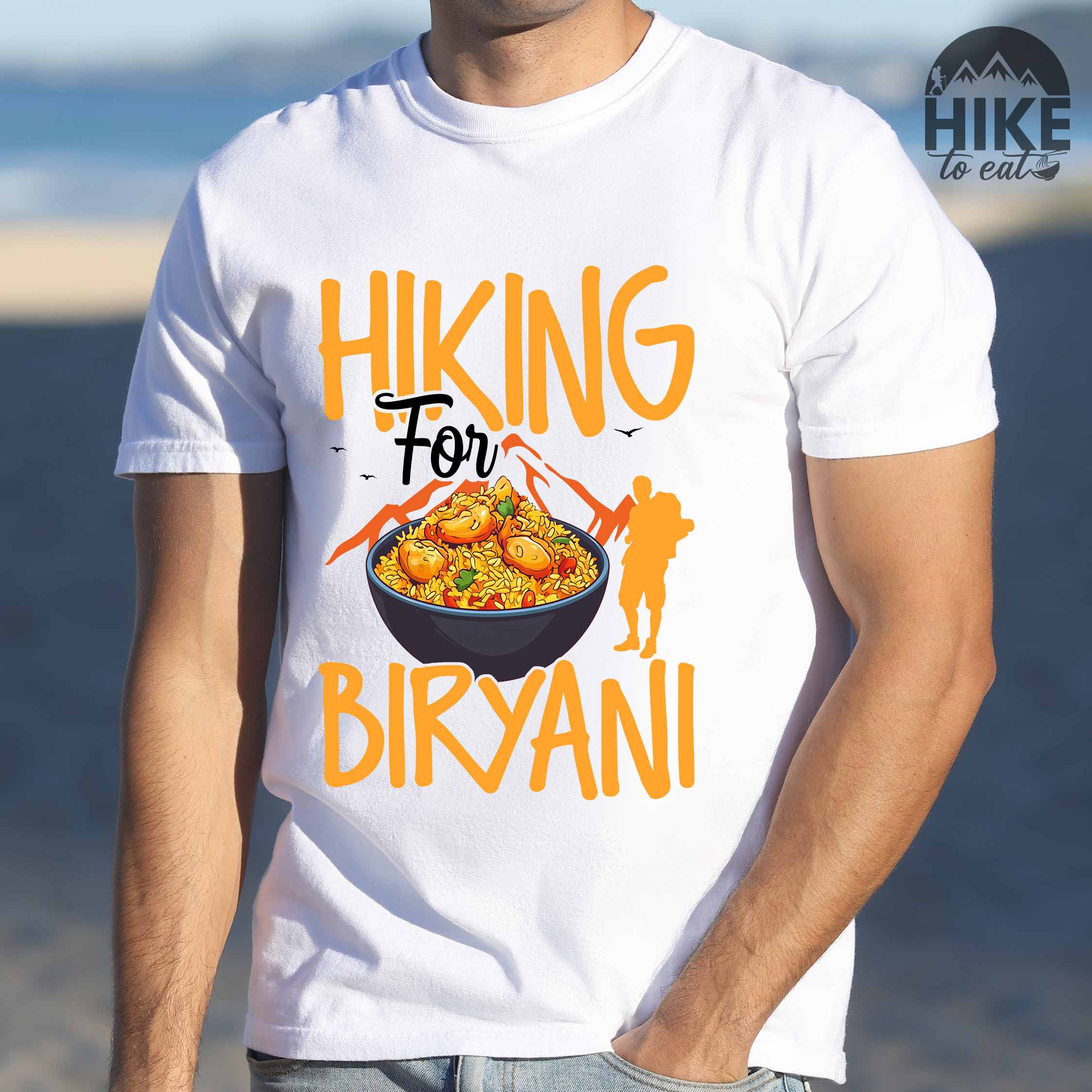 Man wearing white "Hiking for Biryani" colored vintage tee with bold typography, birds, mountains, illustrated bowl of biryani rice, and backpacker for rice lovers.