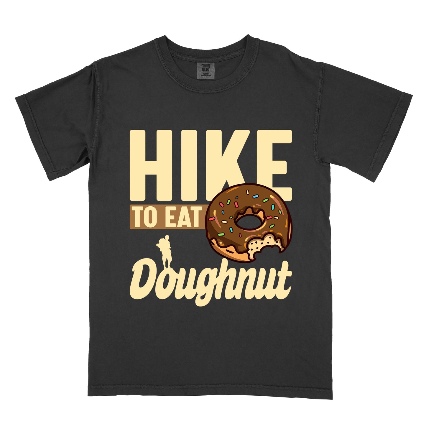 Black t-shirt with cream and tan text reading "HIKE TO EAT Doughnut". "HIKE" appears in large cream letters at the top, "TO EAT" on a tan rectangular background in the middle, and "Doughnut" in cream script at the bottom. Features a chocolate frosted doughnut with colorful sprinkles and a bite taken out of it on the right side, and a small cream silhouette of a hiker on the left. 