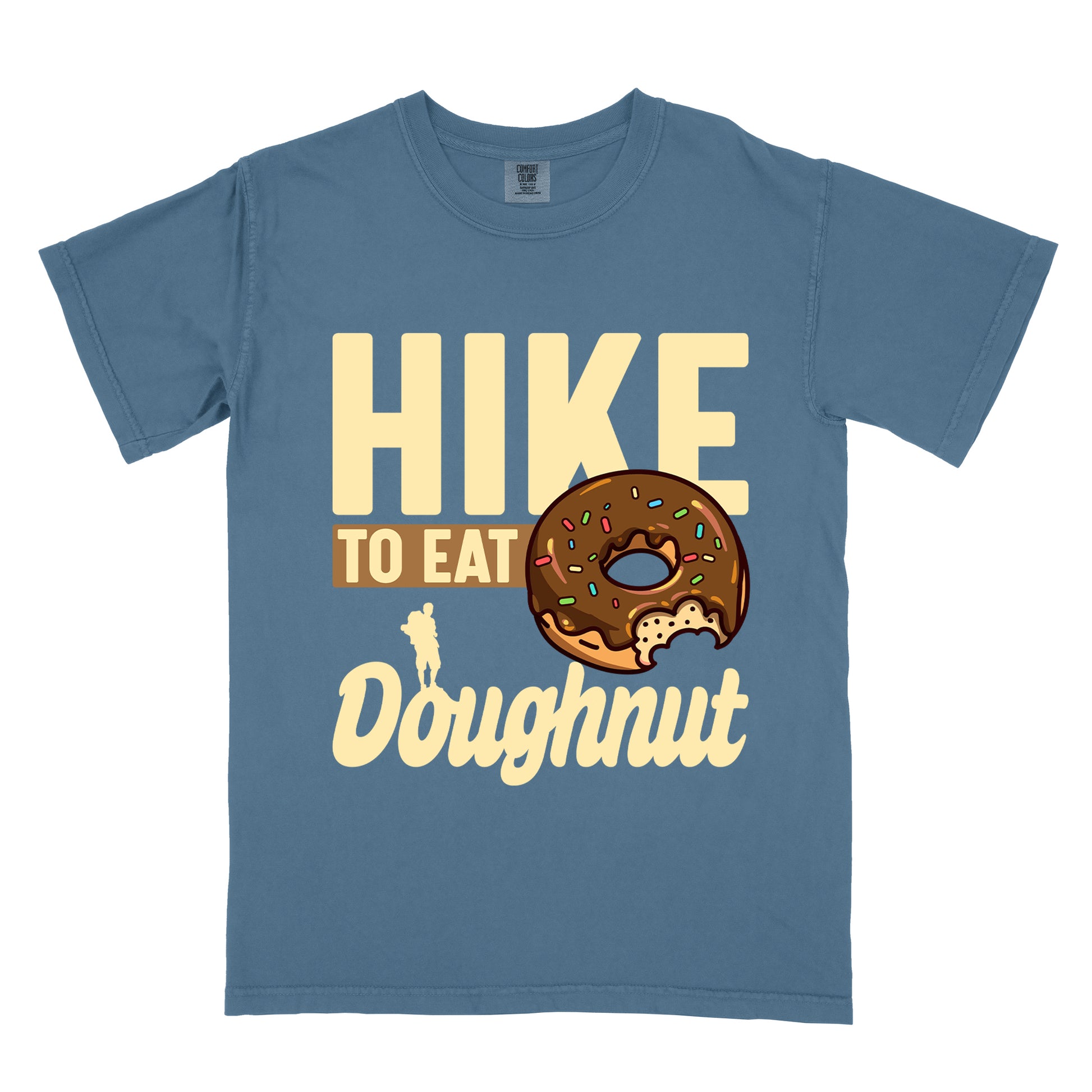 Blue Jean (Denim Blue) t-shirt with cream and tan text reading "HIKE TO EAT Doughnut". "HIKE" appears in large cream letters at the top, "TO EAT" on a tan rectangular background in the middle, and "Doughnut" in cream script at the bottom. Features a chocolate frosted doughnut with colorful sprinkles and a bite taken out of it on the right side, and a small cream silhouette of a hiker on the left. 