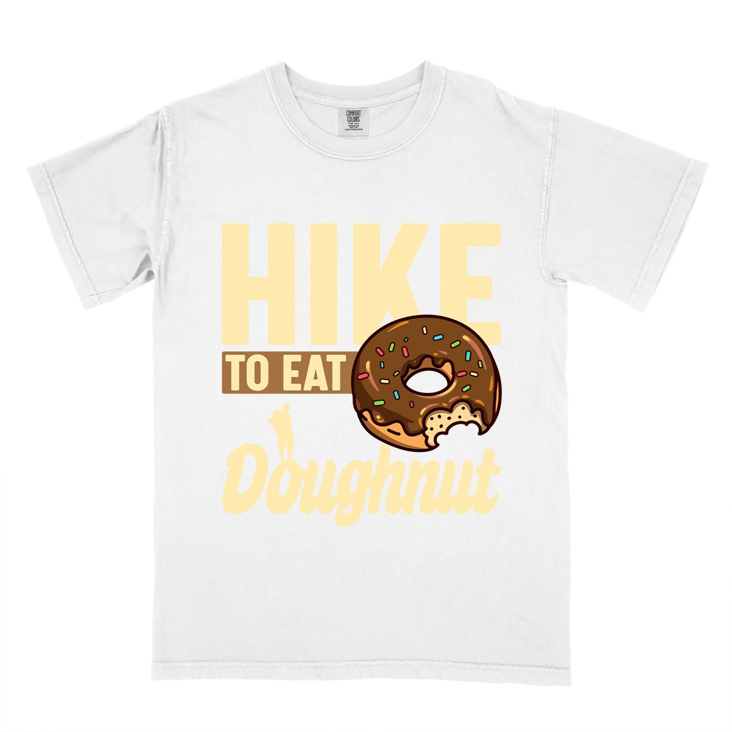 White t-shirt with cream and tan text reading "HIKE TO EAT Doughnut". "HIKE" appears in large cream letters at the top, "TO EAT" on a tan rectangular background in the middle, and "Doughnut" in cream script at the bottom. Features a chocolate frosted doughnut with colorful sprinkles and a bite taken out of it on the right side, and a small cream silhouette of a hiker on the left. 