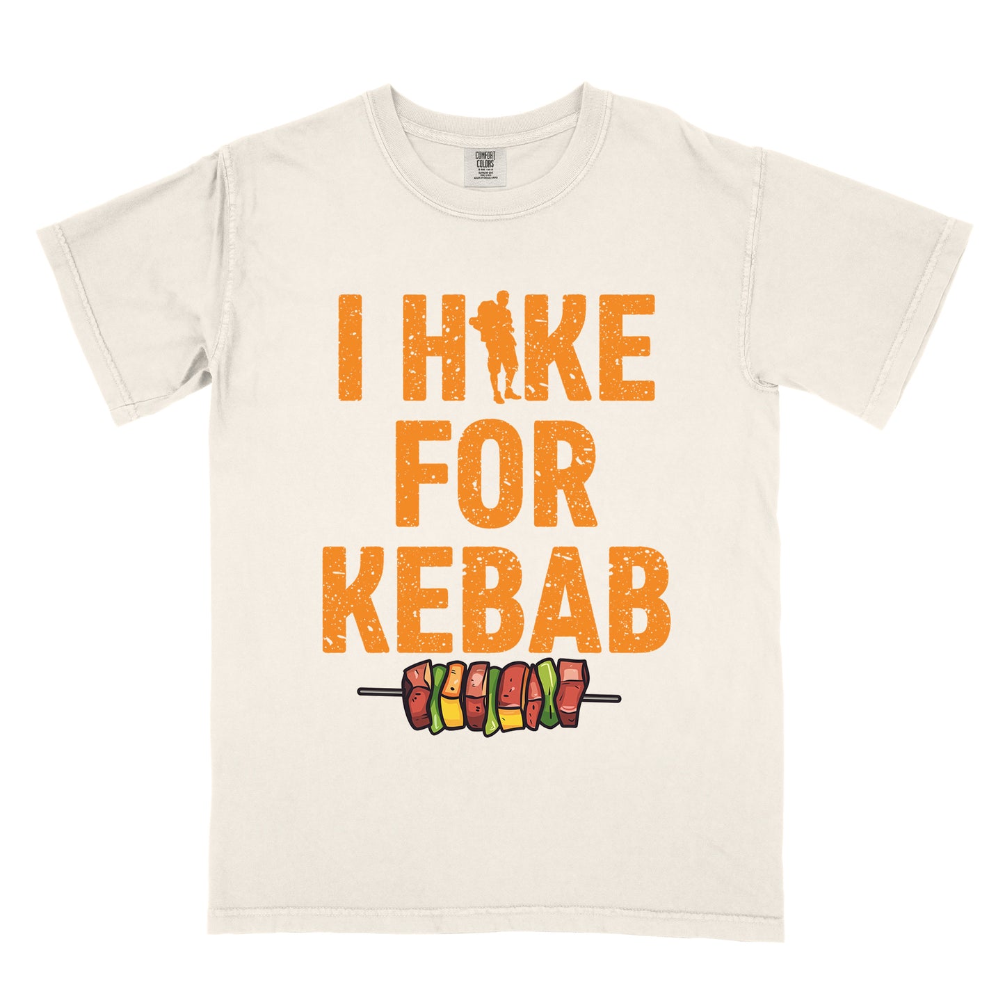 Ivory (Cream White) t-shirt with orange distressed text reading "I HIKE FOR KEBAB". "I HIKE" appears at the top with a hiker silhouette integrated into the letter "I", "FOR" in the middle, and "KEBAB" at the bottom. Below the text is a colorful illustration of a kebab skewer with meat and vegetables.