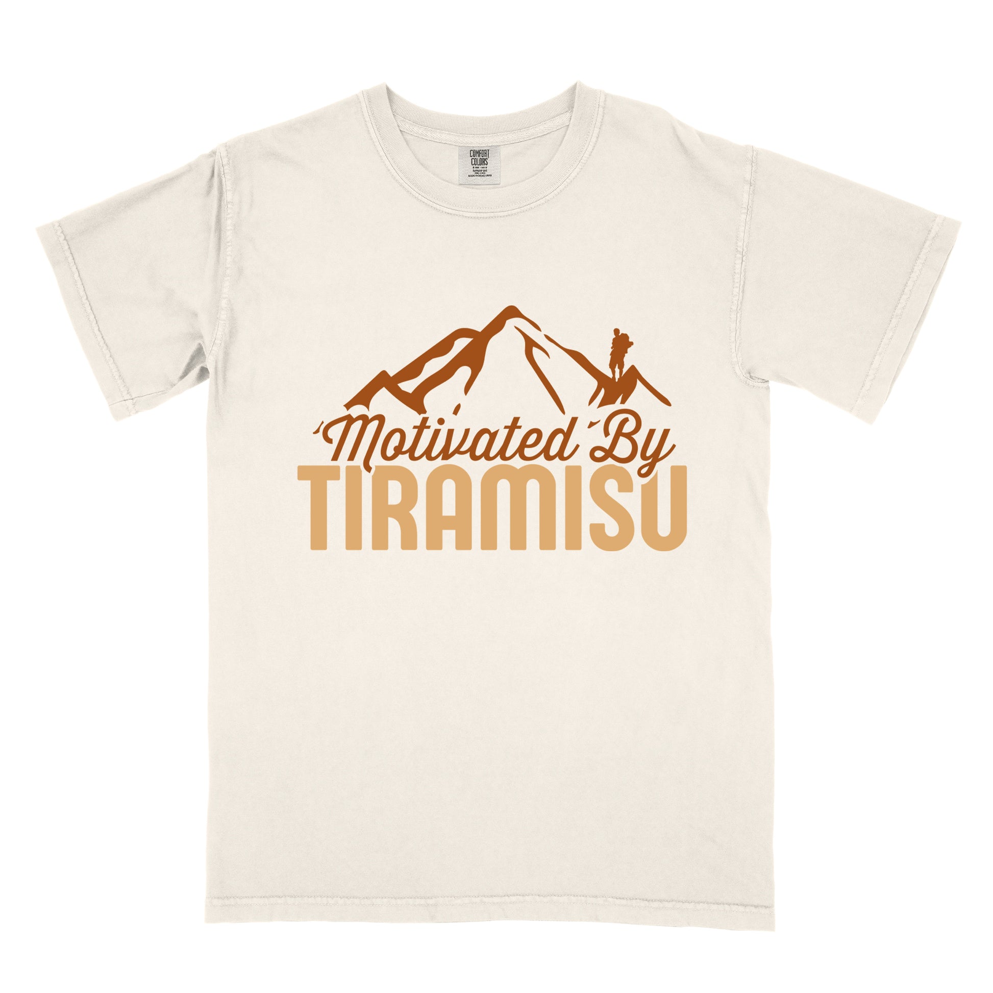 Ivory (Cream White) t-shirt with brown and gold text reading "Motivated By TIRAMISU". "Motivated By" appears in brown script underneath a brown mountain silhouette with a small hiker figure on the peak, and "TIRAMISU" in large gold letters at the bottom. The design humorously connects the Italian coffee-flavored dessert as motivation for hiking and outdoor activities.