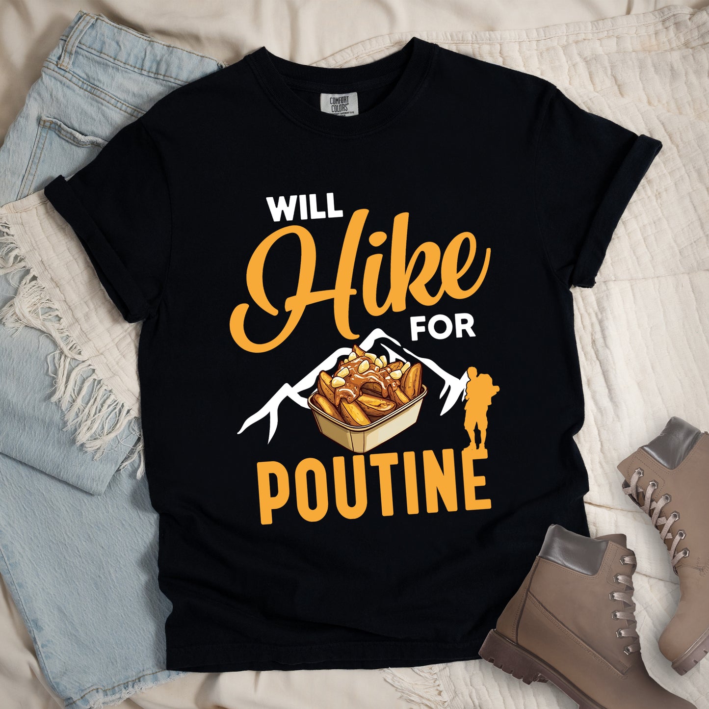 Black t-shirt with orange and white text reading "WILL Hike FOR POUTINE". "WILL" appears in white at the top, "Hike" in large orange script in the middle, "FOR" in white, and "POUTINE" in large orange letters at the bottom. Features a detailed illustration of a container of poutine (french fries with cheese curds and gravy) in the center, white mountain silhouettes behind it, and an orange hiker silhouette on the right. 