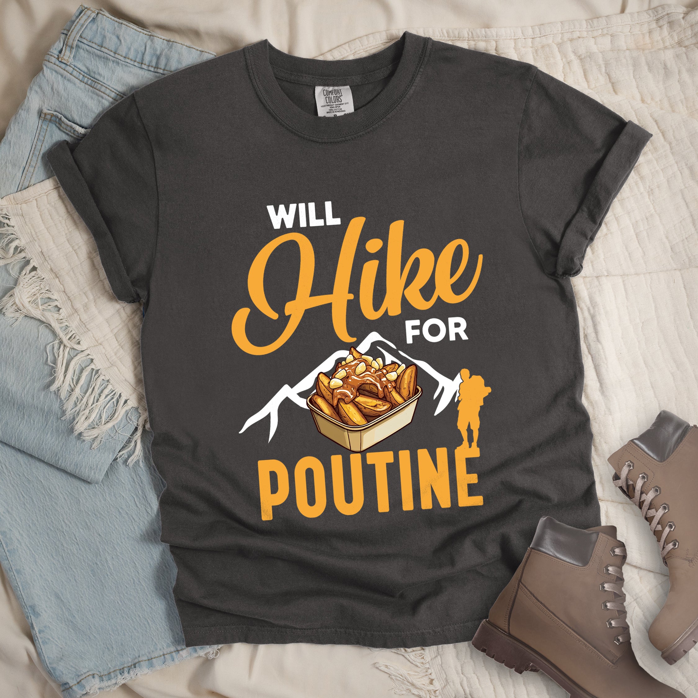 Pepper (Dark Gray) t-shirt with orange and white text reading "WILL Hike FOR POUTINE". "WILL" appears in white at the top, "Hike" in large orange script in the middle, "FOR" in white, and "POUTINE" in large orange letters at the bottom. Features a detailed illustration of a container of poutine (french fries with cheese curds and gravy) in the center, white mountain silhouettes behind it, and an orange hiker silhouette on the right. 