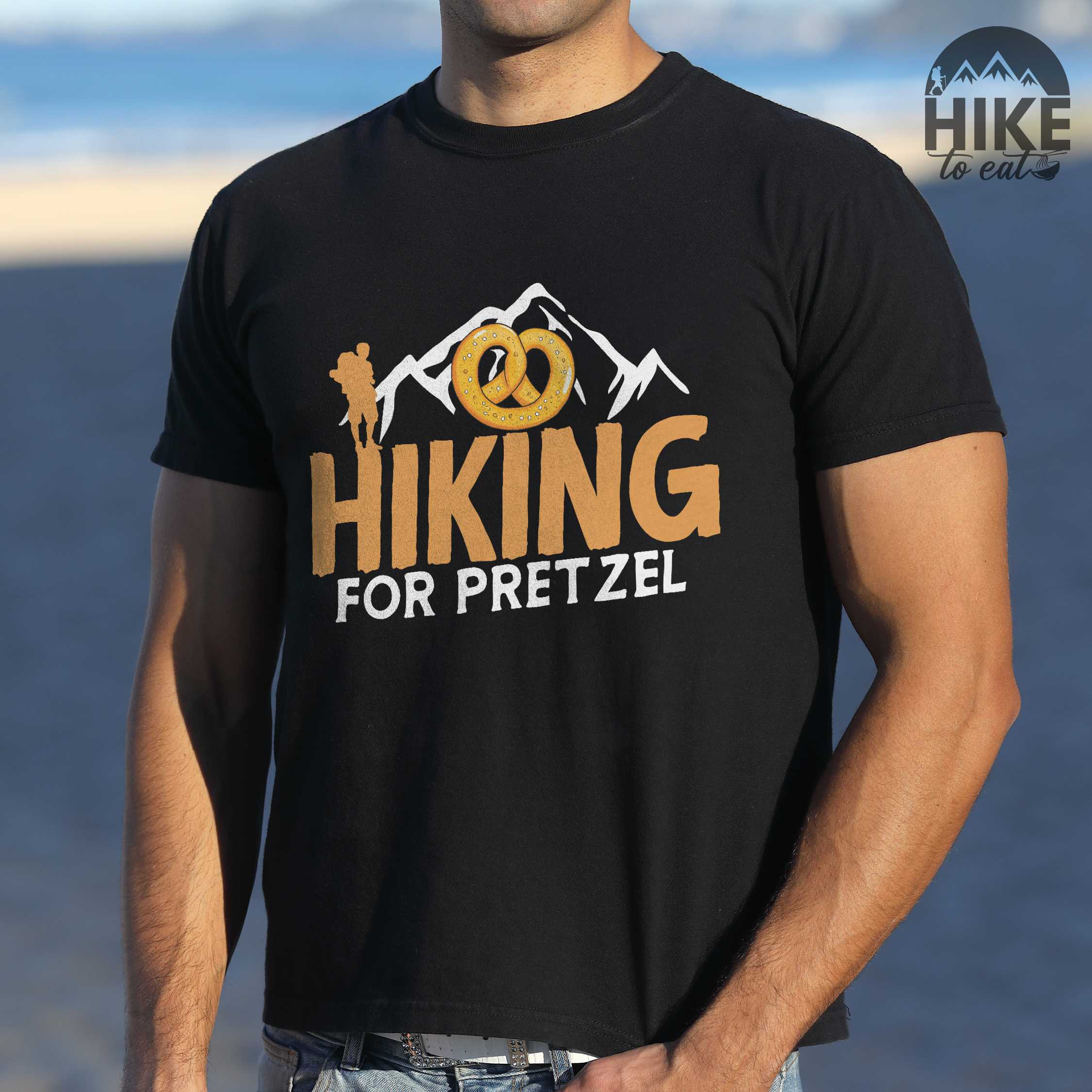 Man wearing black "Hiking for pretzel" colored vintage tee with bold typography, mountains, birds, and illustrated pretzel for baked pretzel lovers