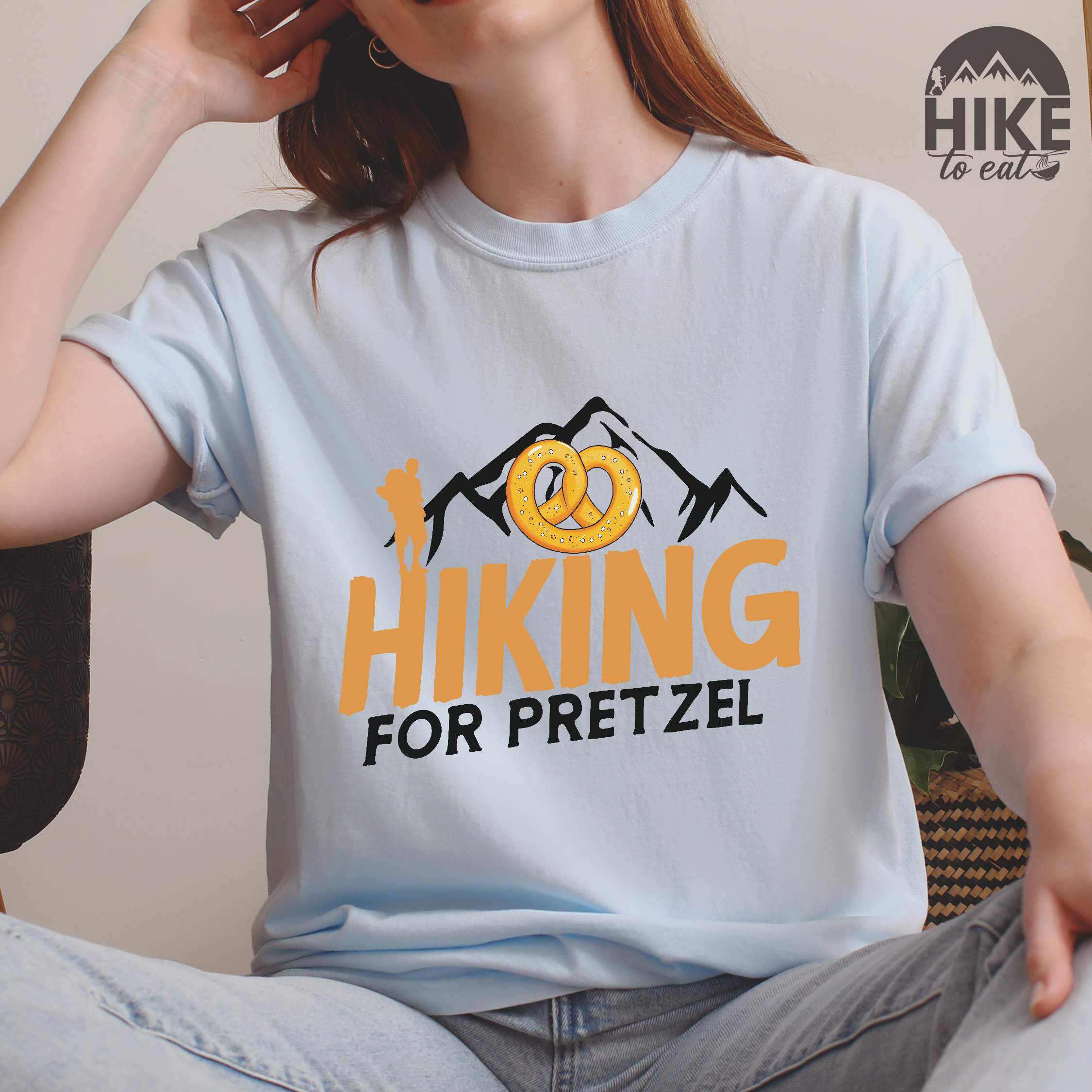 Woman wearing chambray "Hiking for pretzel" colored vintage tee with bold typography, mountains, birds, and illustrated pretzel for baked pretzel lovers