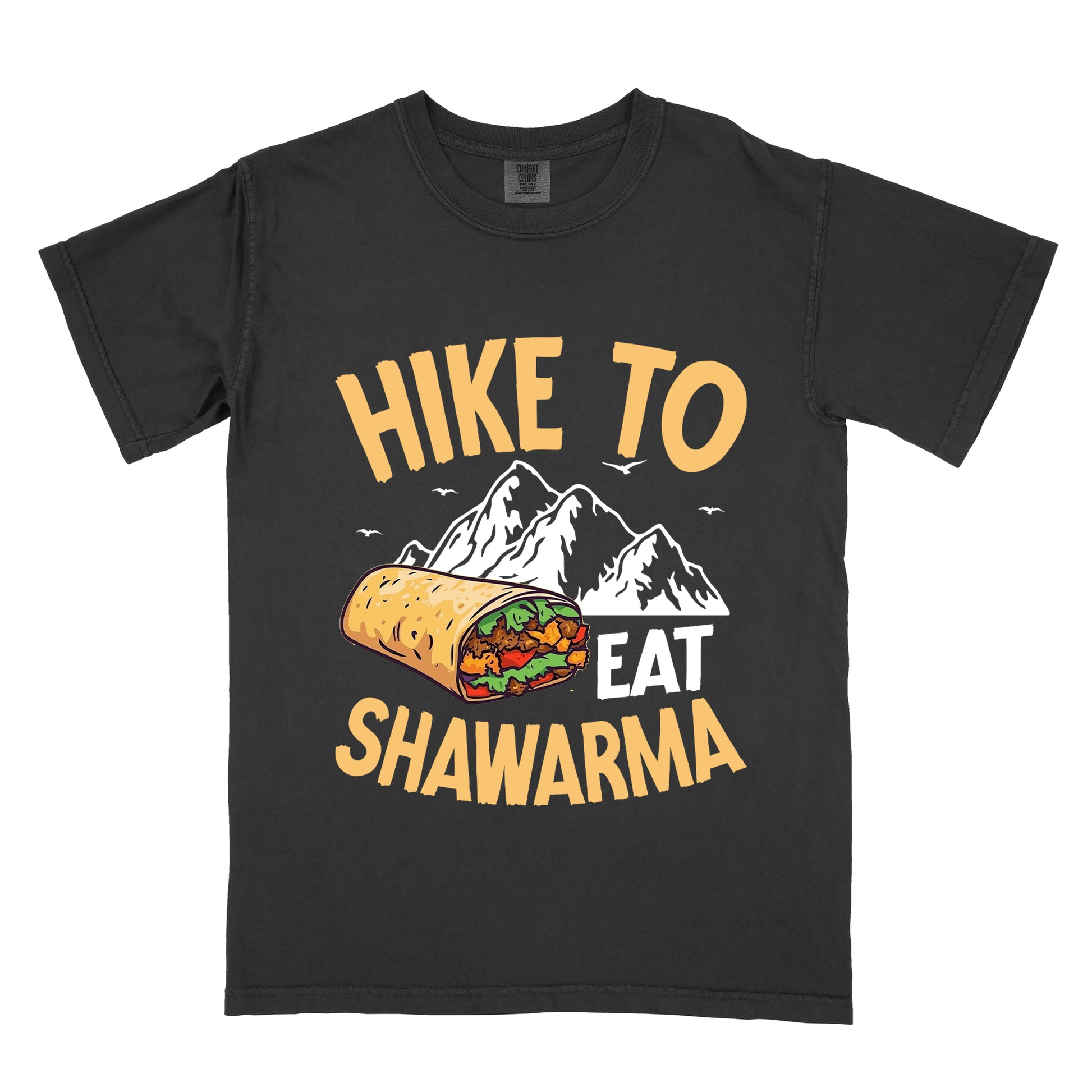 Black t-shirt with golden yellow and white text reading "HIKE TO EAT SHAWARMA". "HIKE TO" appears in golden yellow letters at the top, "EAT" in white in the middle, and "SHAWARMA" in golden yellow at the bottom. Features a detailed illustration of a shawarma wrap with visible meat and vegetables, white mountain silhouettes with small bird silhouettes in the background. 
