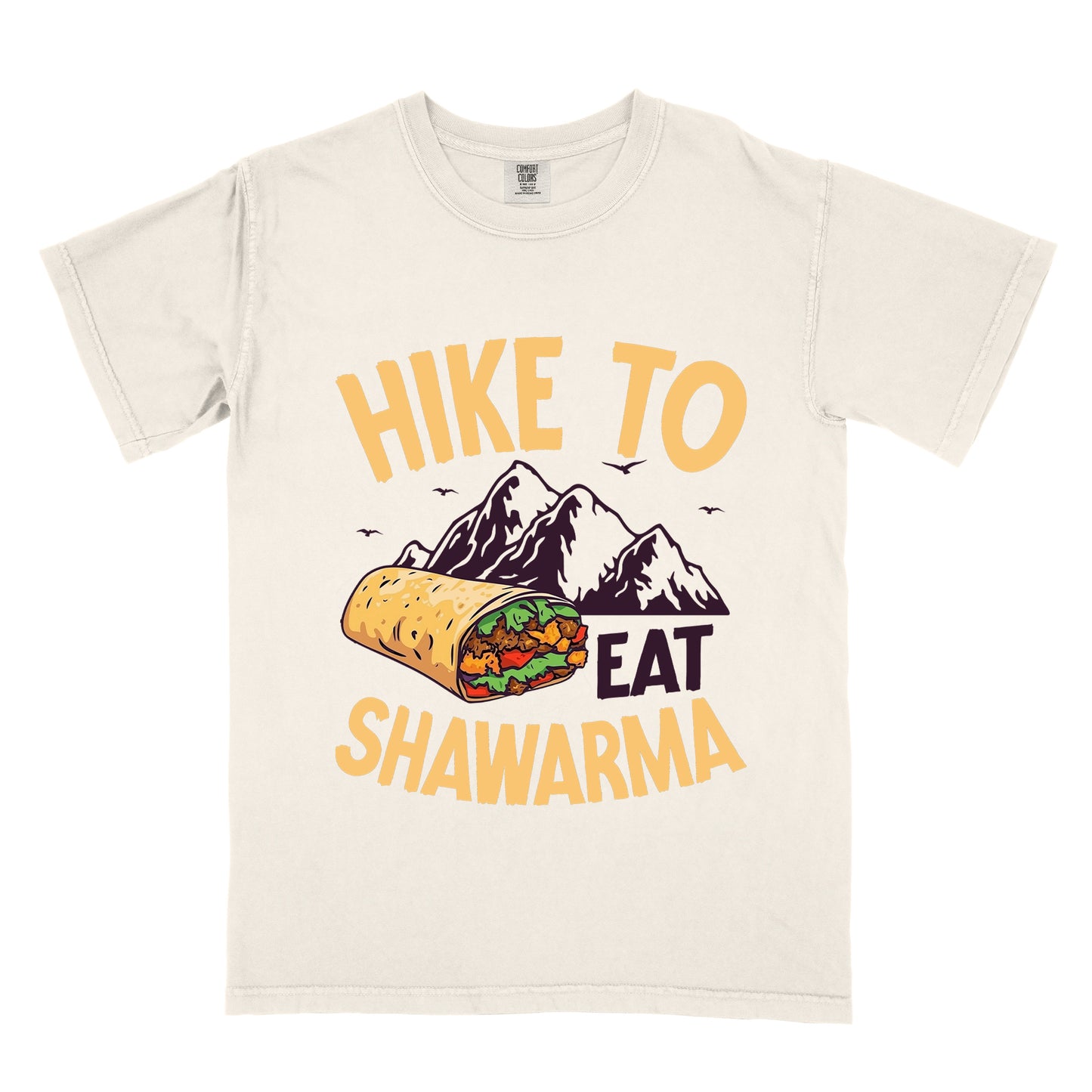 Ivory (Cream White) t-shirt with golden yellow and deep purple text reading "HIKE TO EAT SHAWARMA". "HIKE TO" appears in golden yellow letters at the top, "EAT" in deep purple in the middle, and "SHAWARMA" in golden yellow at the bottom. Features a detailed illustration of a shawarma wrap with visible meat and vegetables, deep purple mountain silhouettes with small bird silhouettes in the background. 