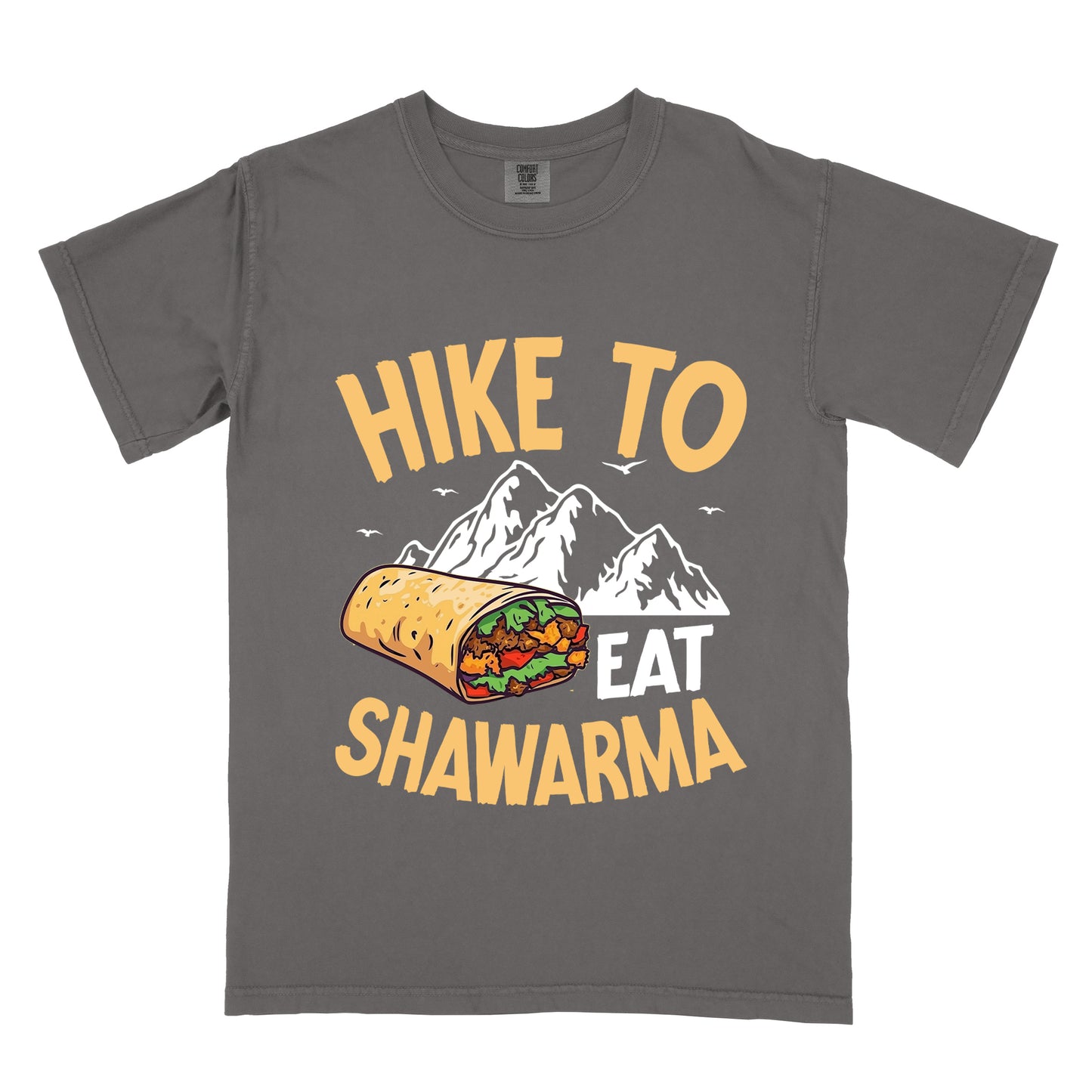 Pepper (Dark Gray) t-shirt with golden yellow and white text reading "HIKE TO EAT SHAWARMA". "HIKE TO" appears in golden yellow letters at the top, "EAT" in white in the middle, and "SHAWARMA" in golden yellow at the bottom. Features a detailed illustration of a shawarma wrap with visible meat and vegetables, white mountain silhouettes with small bird silhouettes in the background. 