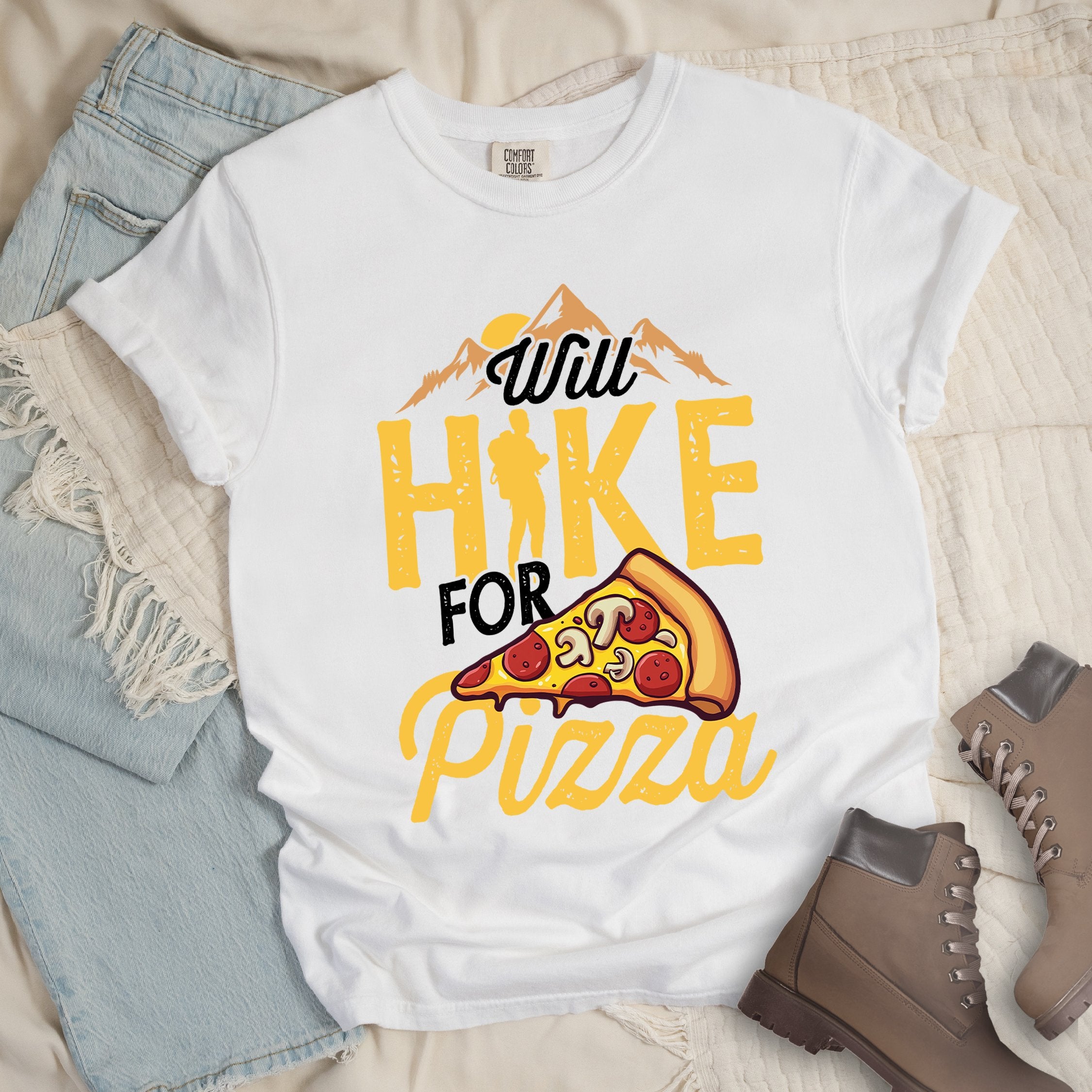 White shirt featuring Hiking design of mountains with a sunrise behind and a slice of pizza in front of the phrase 'Will Hike for Pizza'.