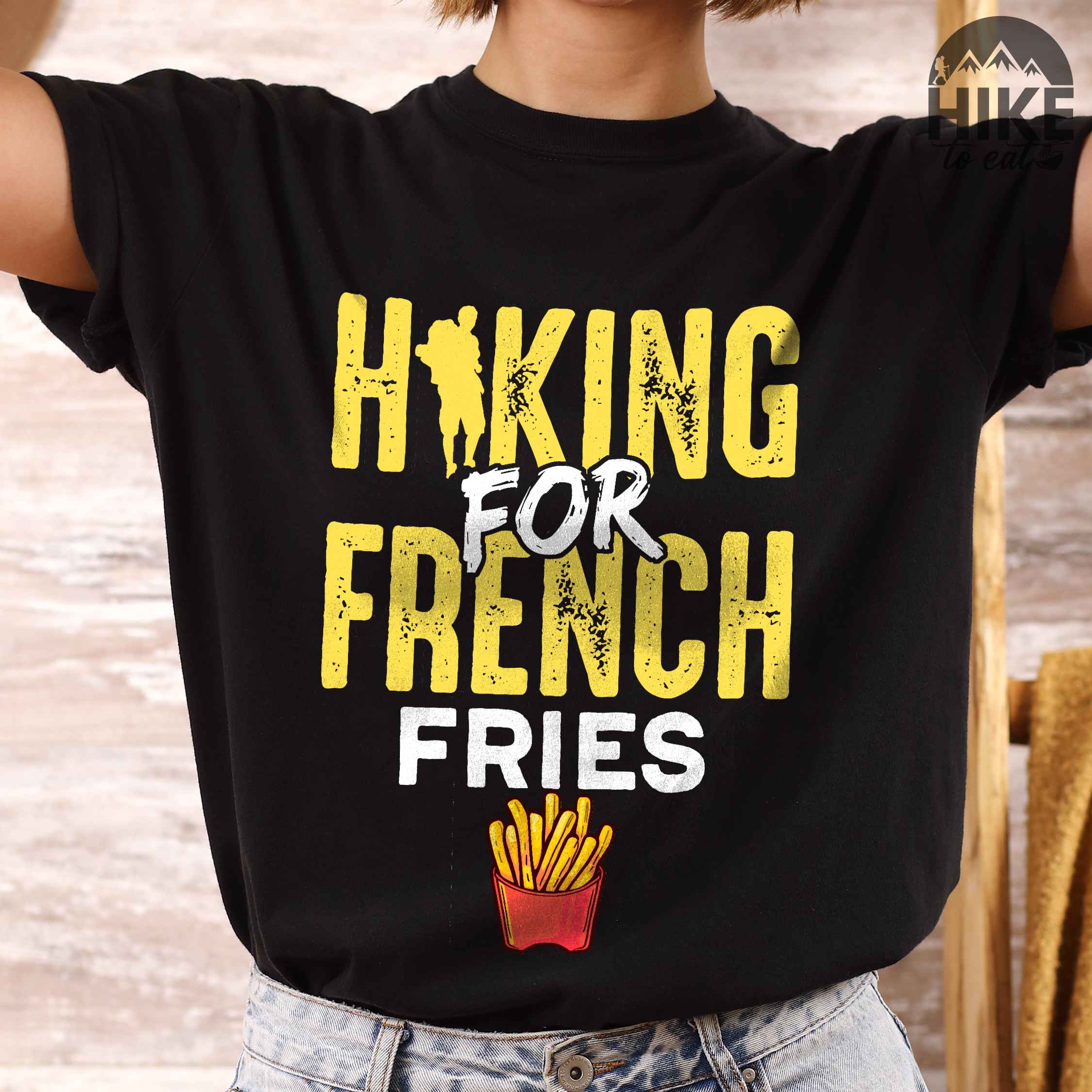 woman wearing black "Hiking for french fries" colored vintage tee with bold typography, mountains, illustrated fries, and backpacker for comfort food enthusiasts.