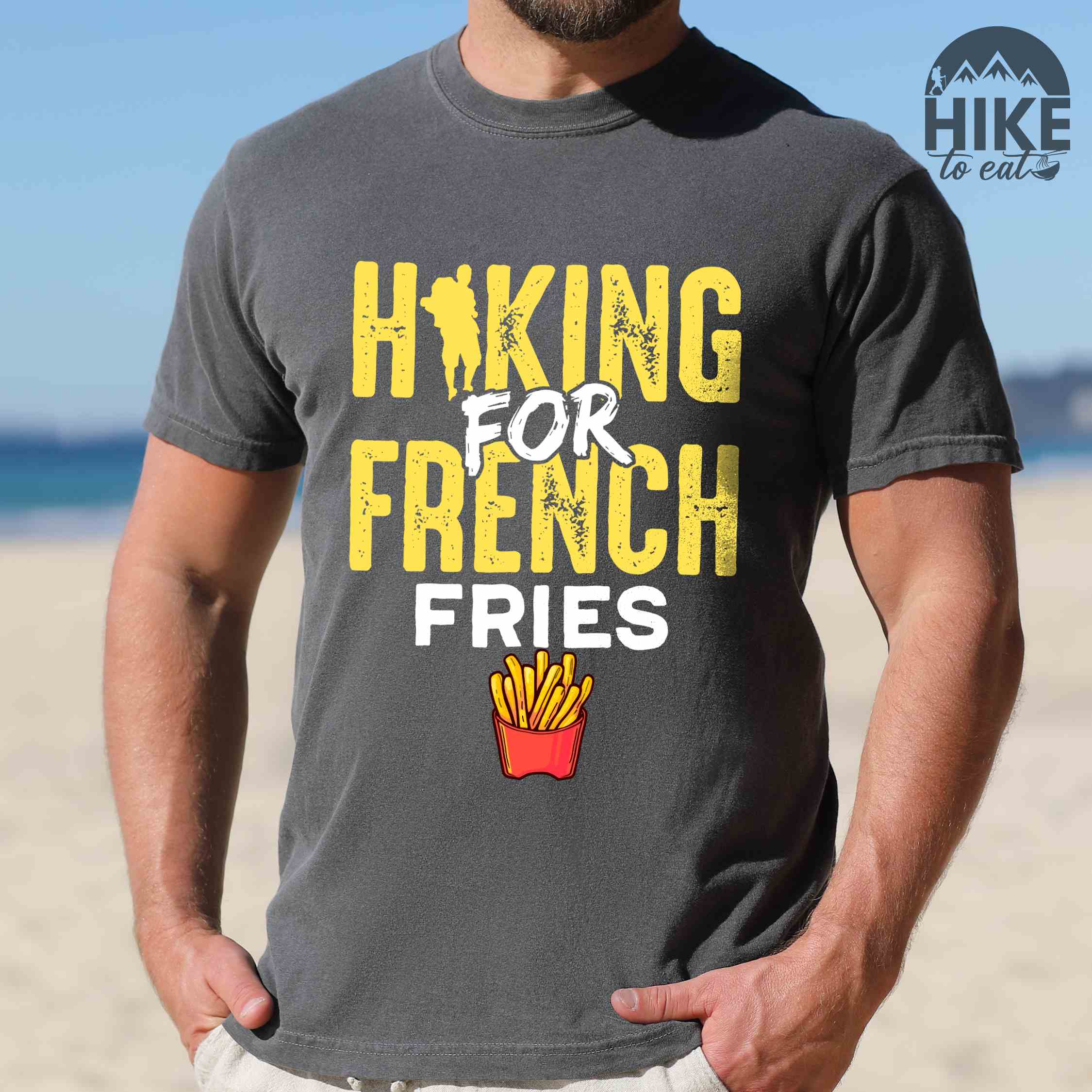 Man wearing pepper "Hiking for french fries" colored vintage tee with bold typography, mountains, illustrated fries, and backpacker for comfort food enthusiasts.