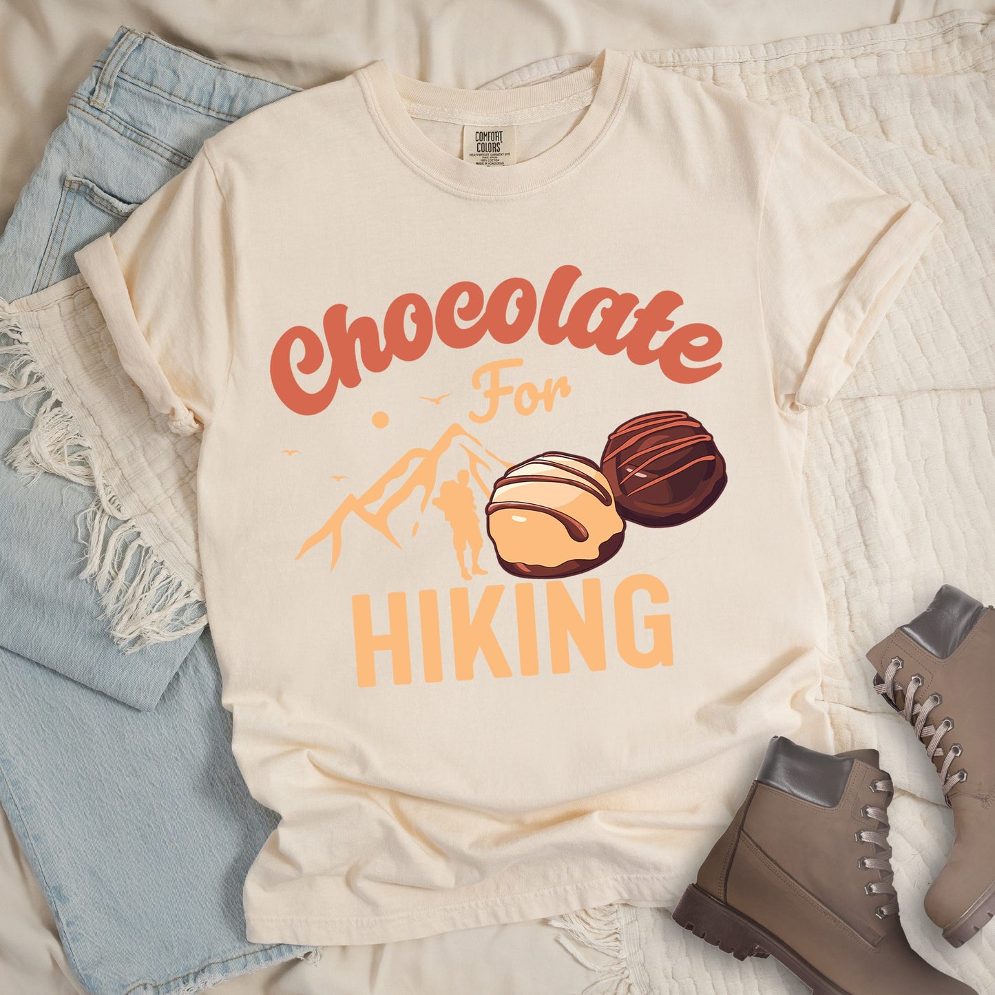 Ivory  shirt with the phrase “Chocolate For Hiking.” Features a mountain outline, hiker silhouette, and two chocolate truffles illustration.