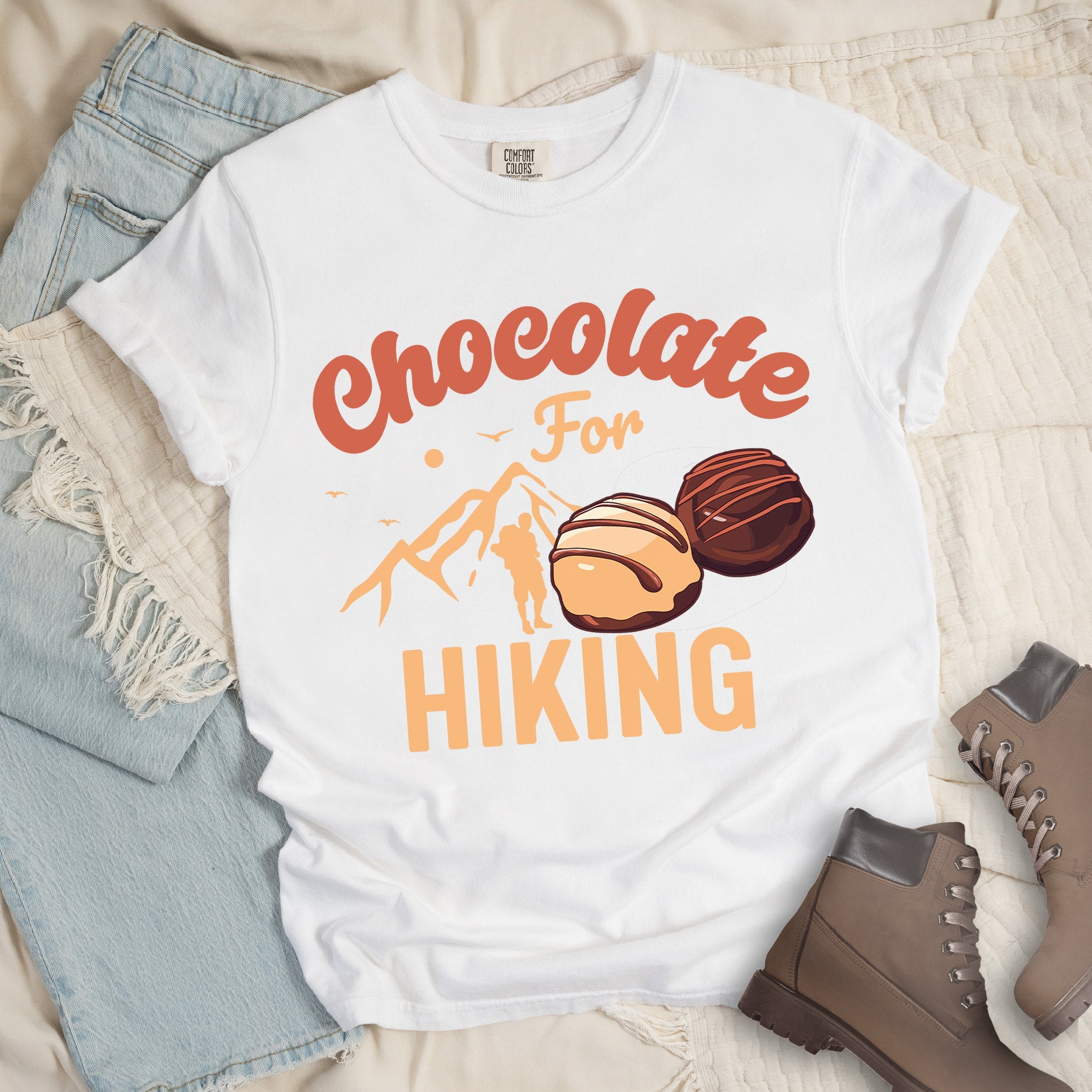 White shirt with the phrase “Chocolate For Hiking.” Features a mountain outline, hiker silhouette, and two chocolate truffles illustration.