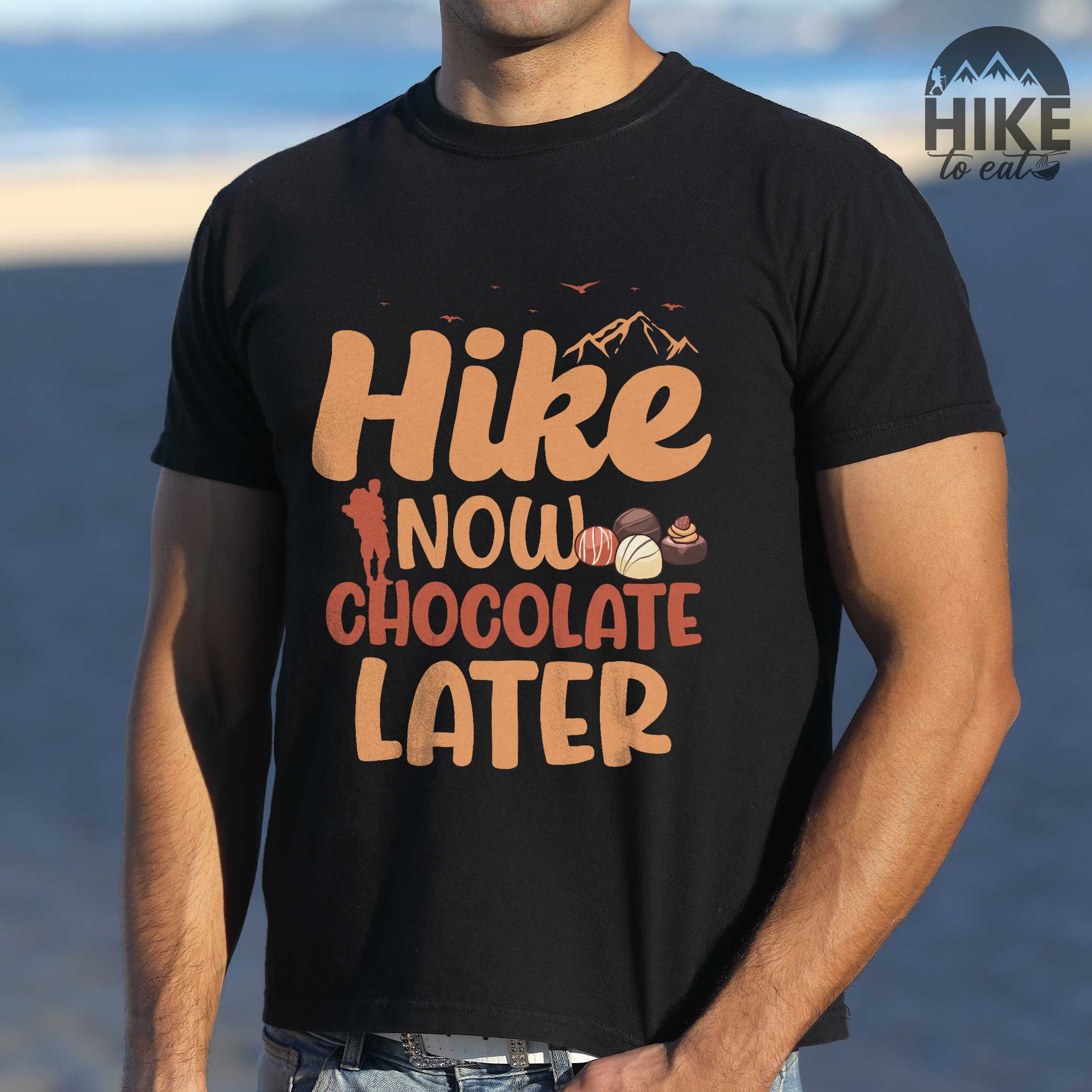 Man wearing black "Hike now chocolate later" colored vintage tee with bold typography, mountains, illustrated a serving of Tiramisu, and perfect for chocolate lovers.