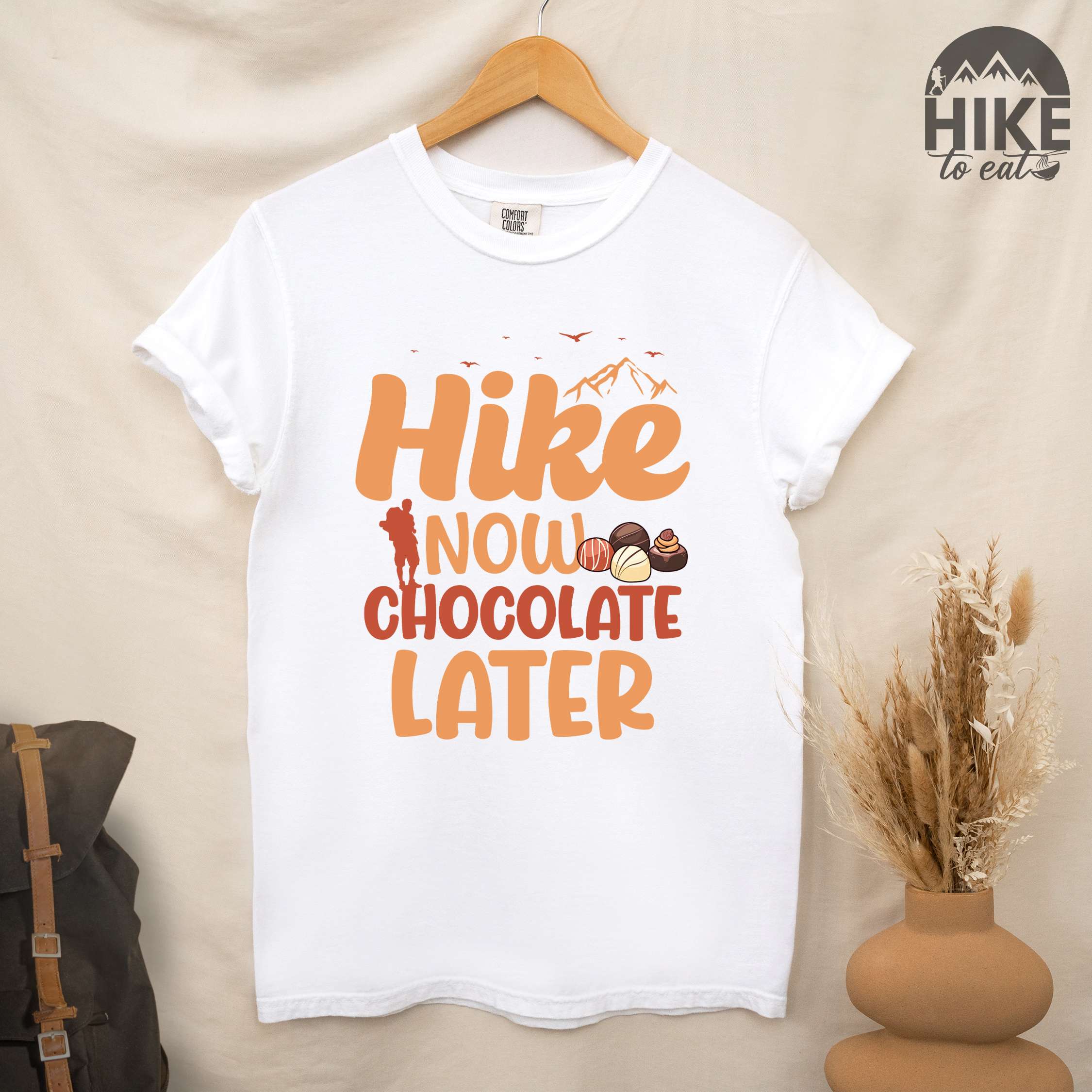 Hanging white "Hike now chocolate later" colored vintage tee with bold typography, mountains, illustrated a serving of Tiramisu, and perfect for chocolate lovers.