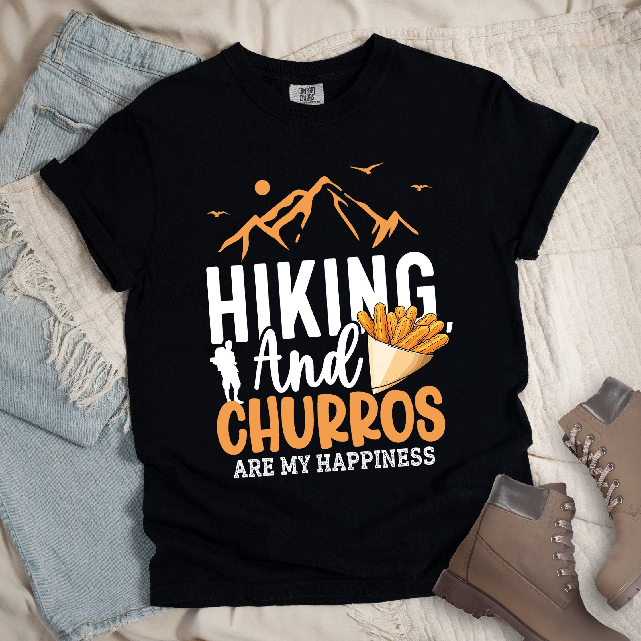 Black shirt with the phrase “Hiking And Churros Are My Happiness.” Features a hiker silhouette, mountains, birds, and a churros cone illustration.