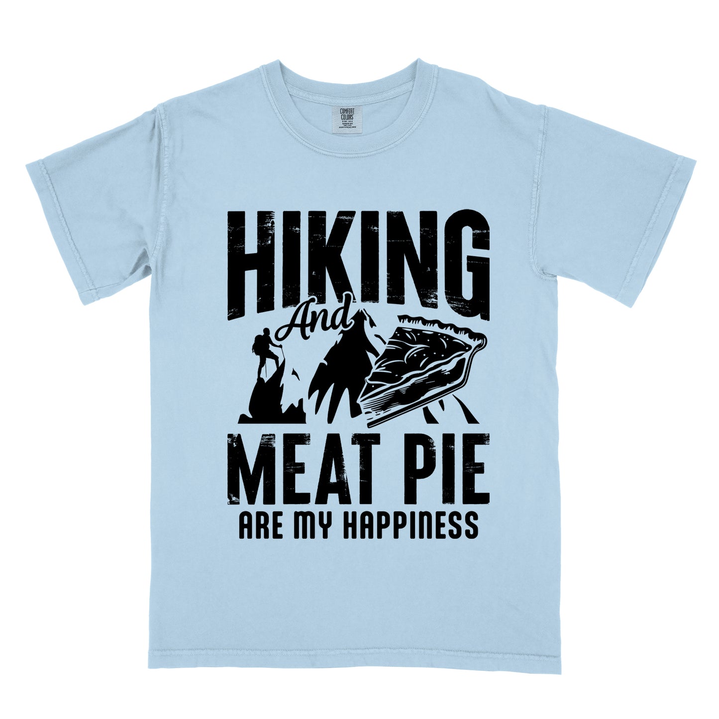 A Chambray (Light Blue) t-shirt featuring black distressed text reading "HIKING And MEAT PIE ARE MY HAPPINESS." Between the words "HIKING" and "MEAT PIE" is a graphic showing a mountain silhouette with a tiny hiker climbing it, alongside an illustration of a slice of meat pie. The design uses only black graphics and text on the Chambray (Light Blue) shirt background in a rugged, vintage style.
